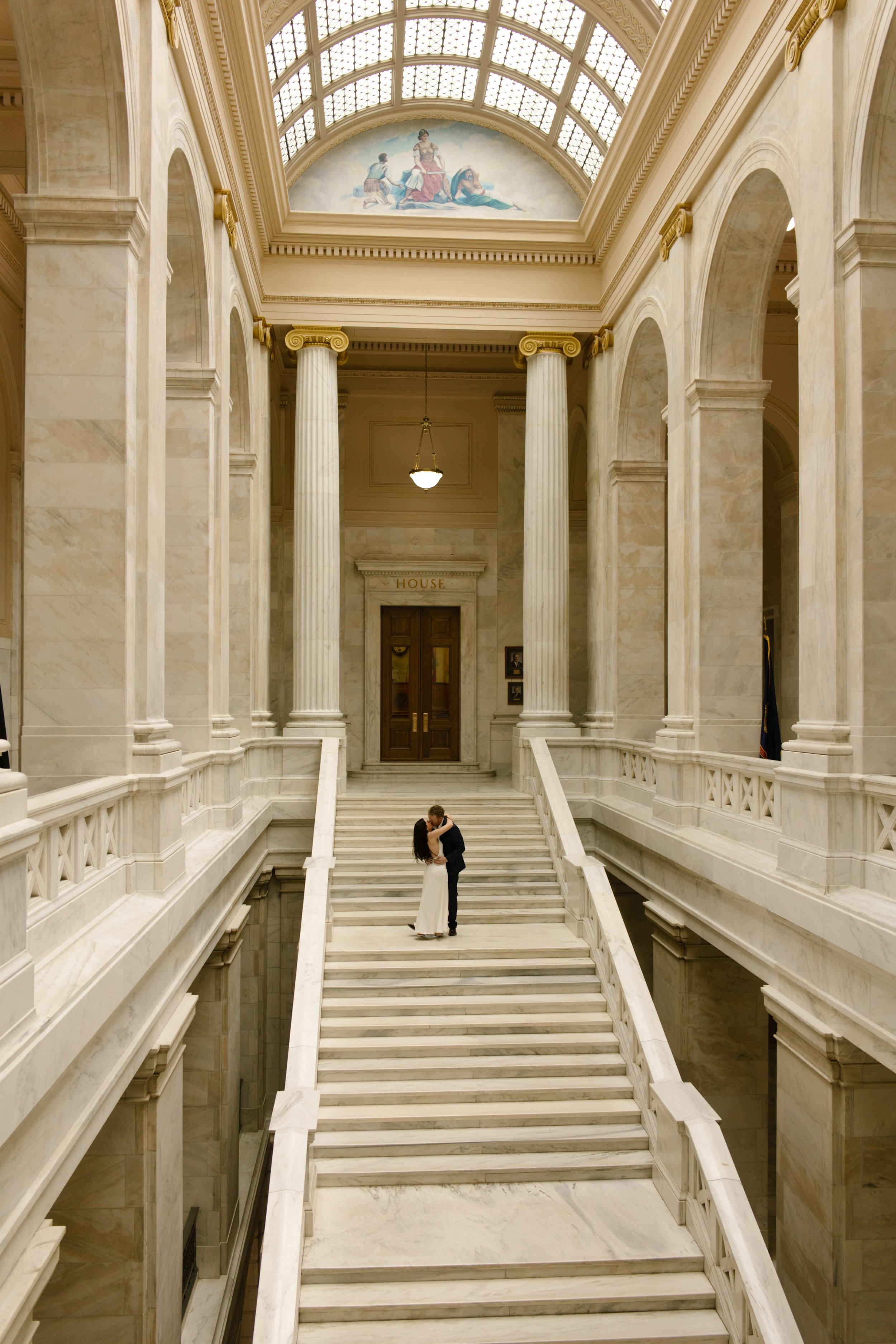 Wide architectural portrait of a couple embracing on the grand staircase at the Little Rock Courthouse