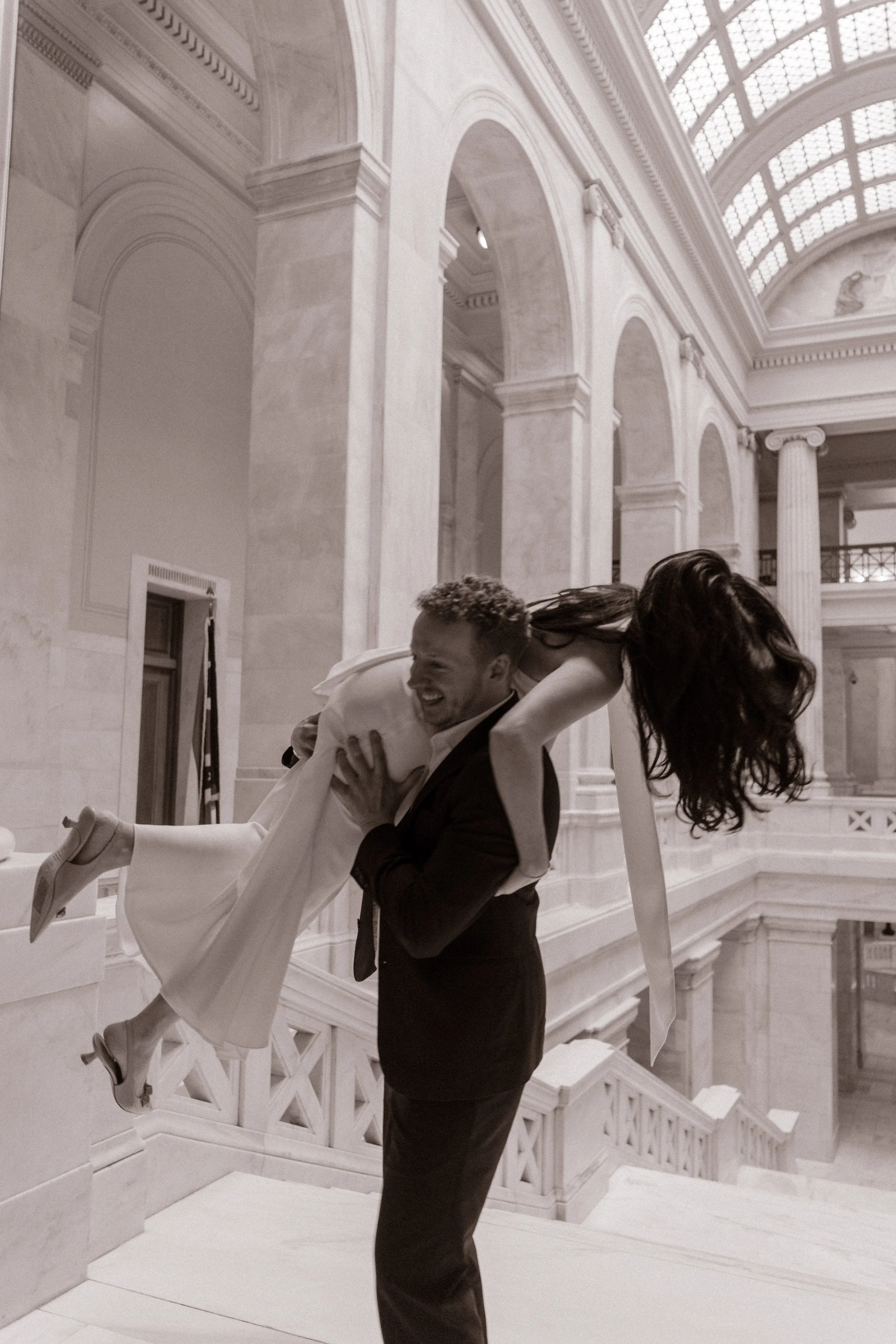 Groom lifts bride in a playful black-and-white portrait inside the Little Rock courthouse rotunda.