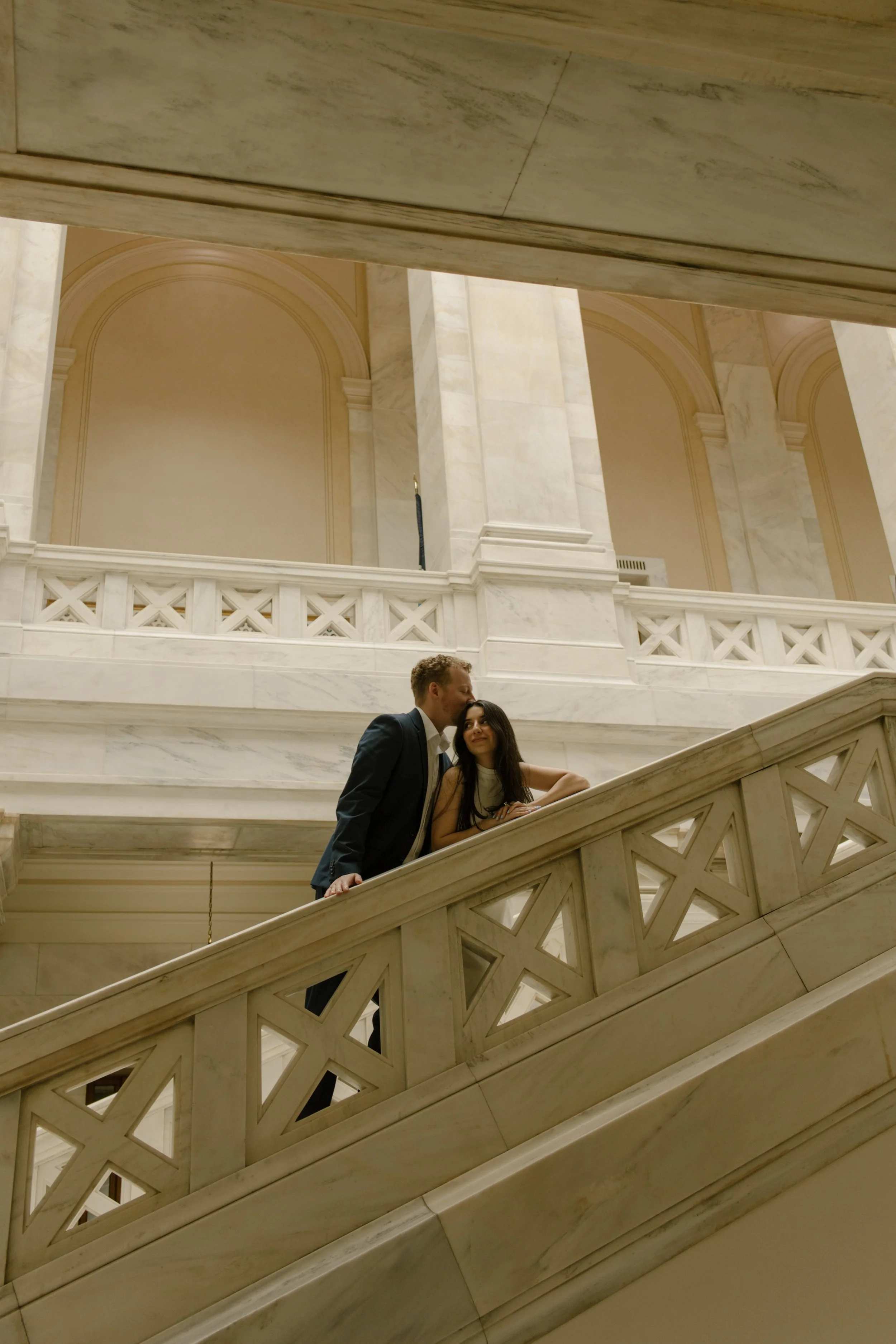 Romantic courthouse portrait framed by marble railings and towering columns as the couple leans together.