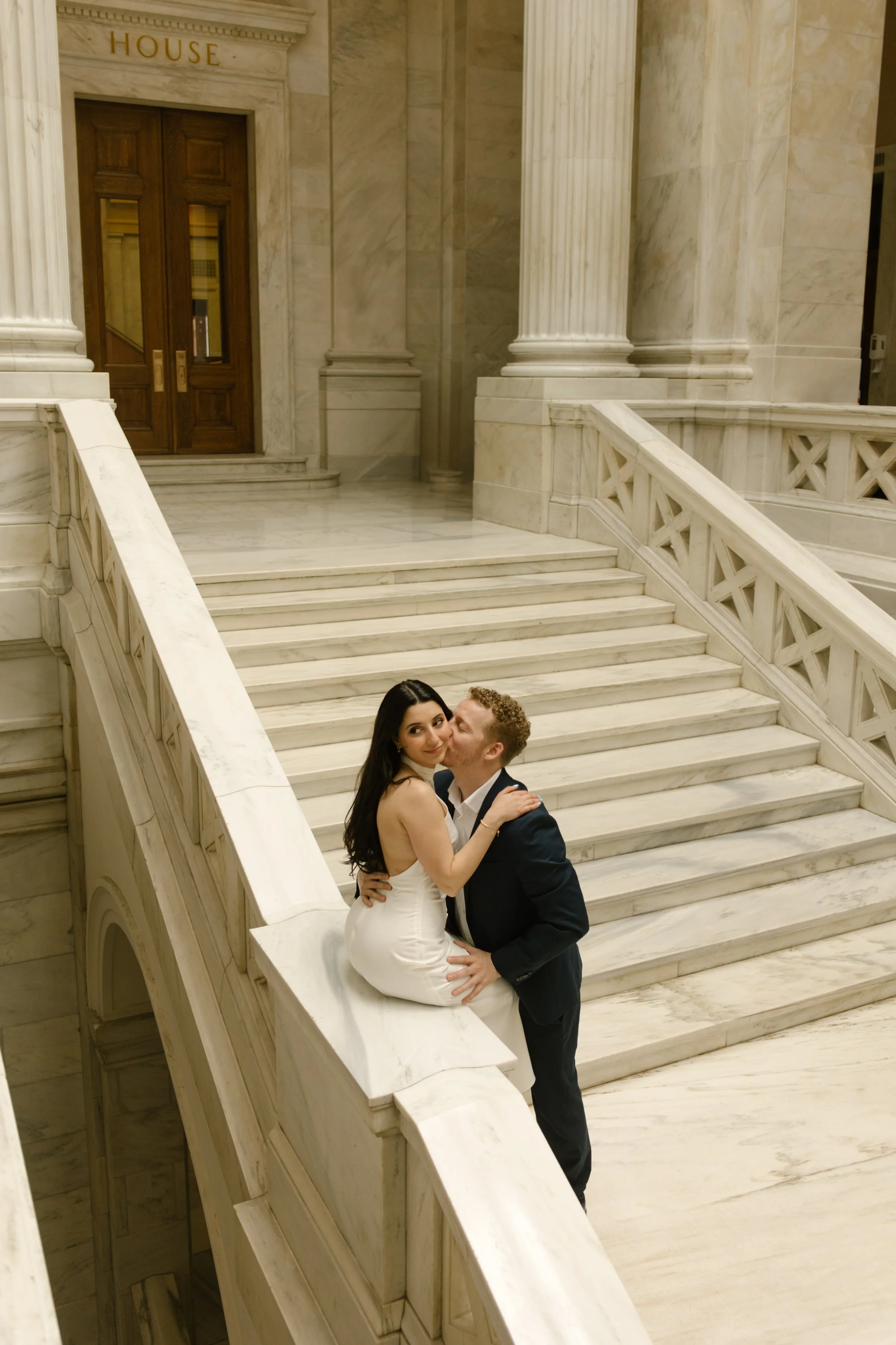 Bride sitting on the courthouse railing while sharing a candid moment with her fiancé