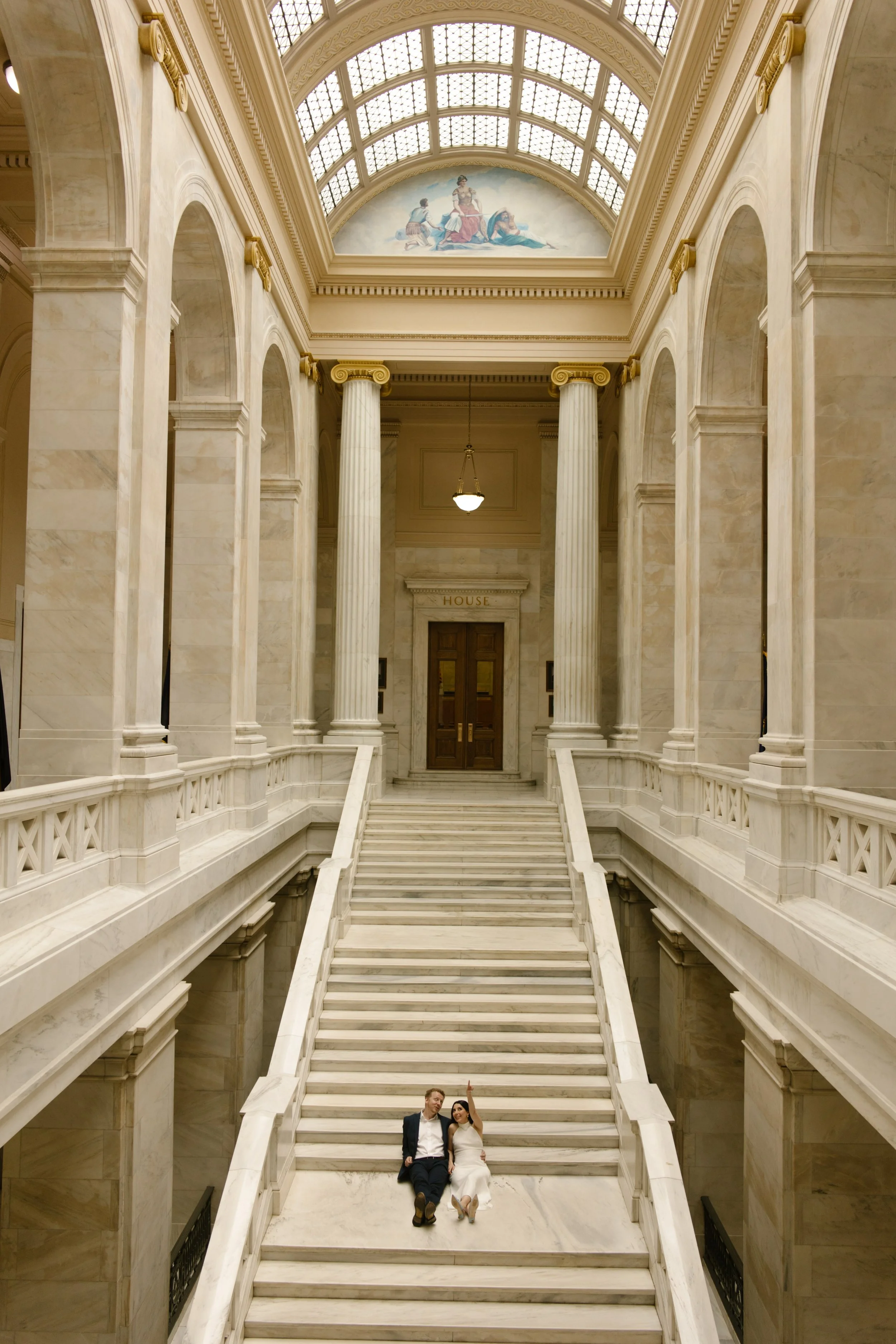 Wide architectural portrait of a couple seated on the grand staircase at the Little Rock Courthouse