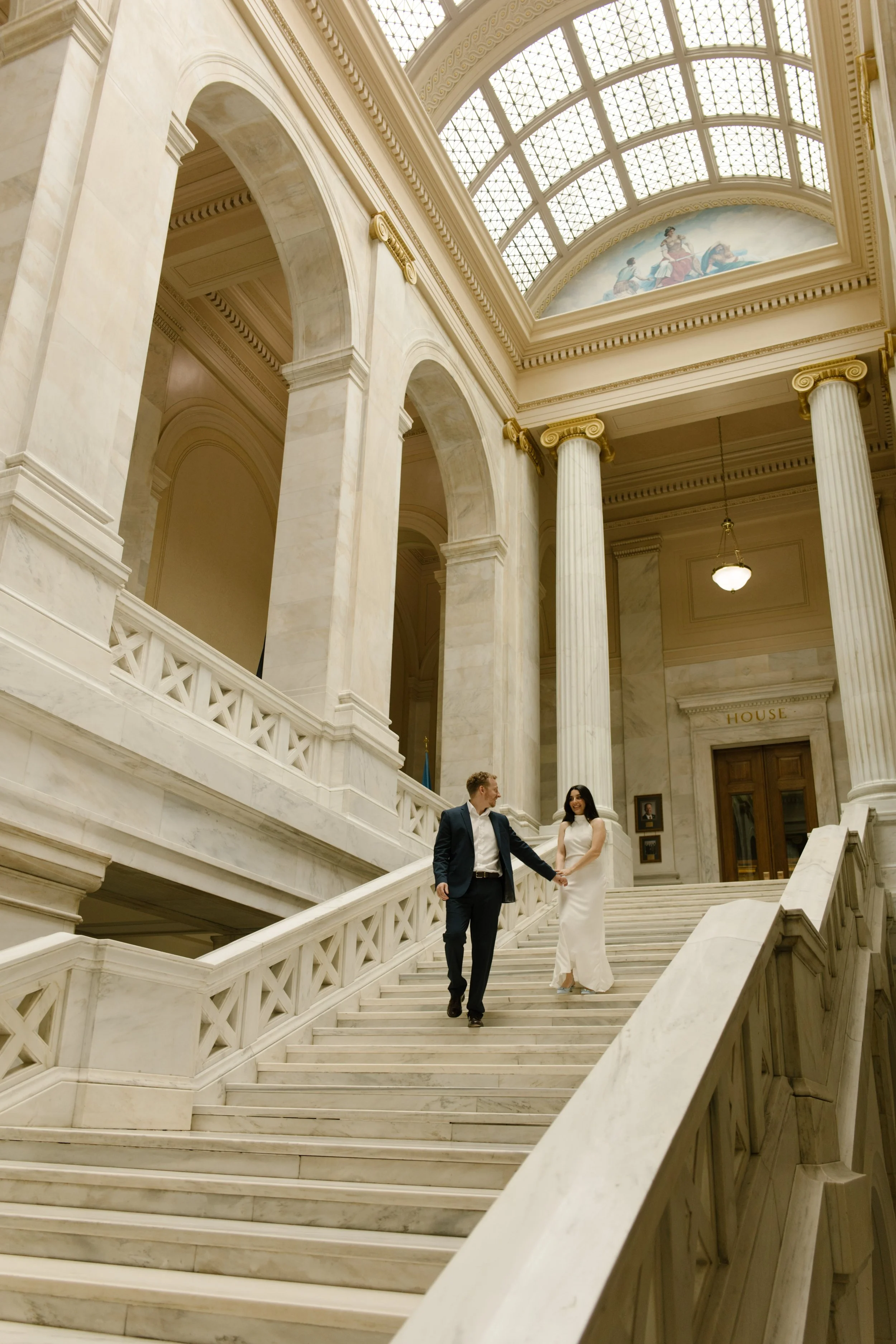 Couple walking hand in hand down the marble staircase during their Little Rock Courthouse engagement session