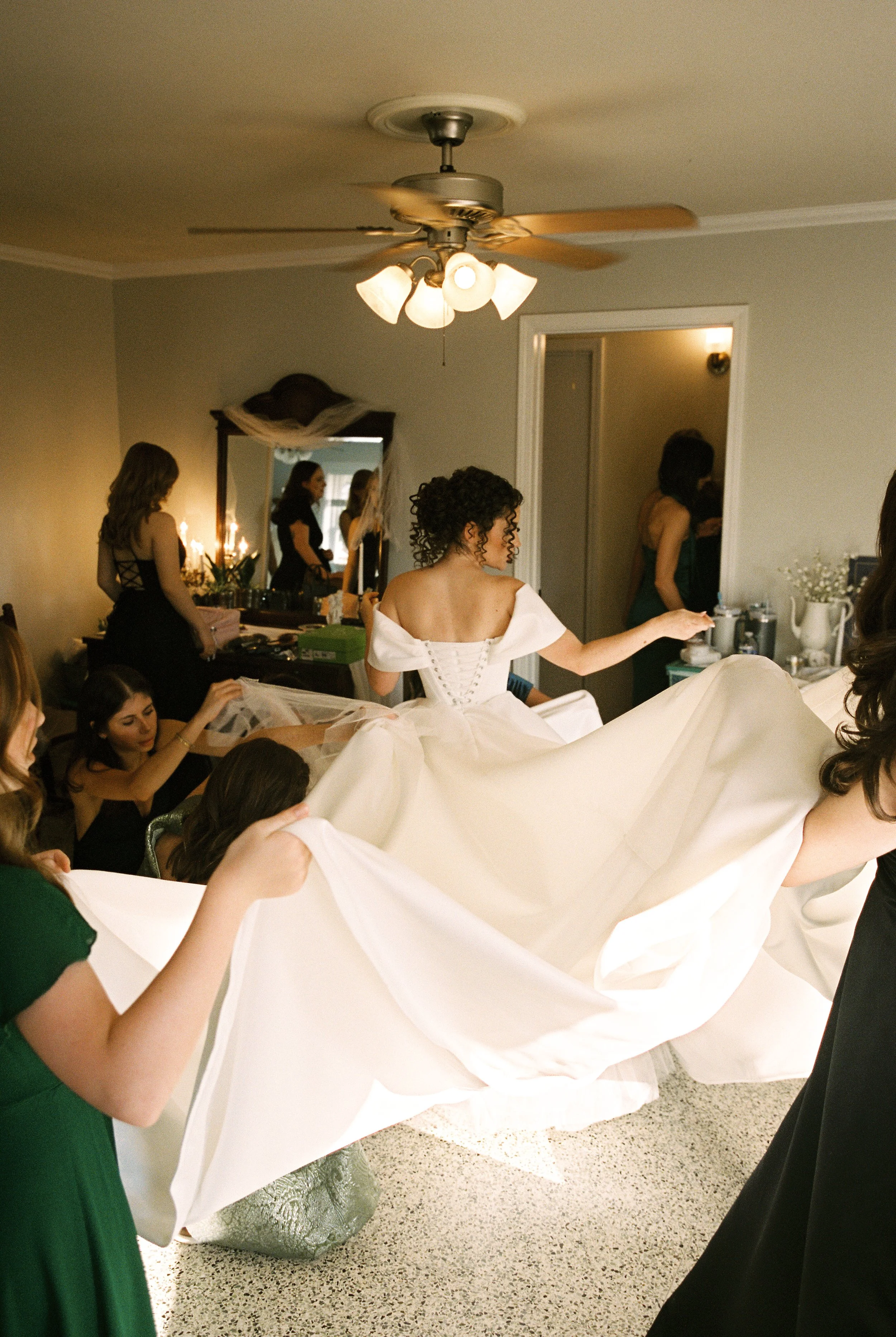 Bridesmaids help arrange the bride’s gown while she prepares before the wedding ceremony.