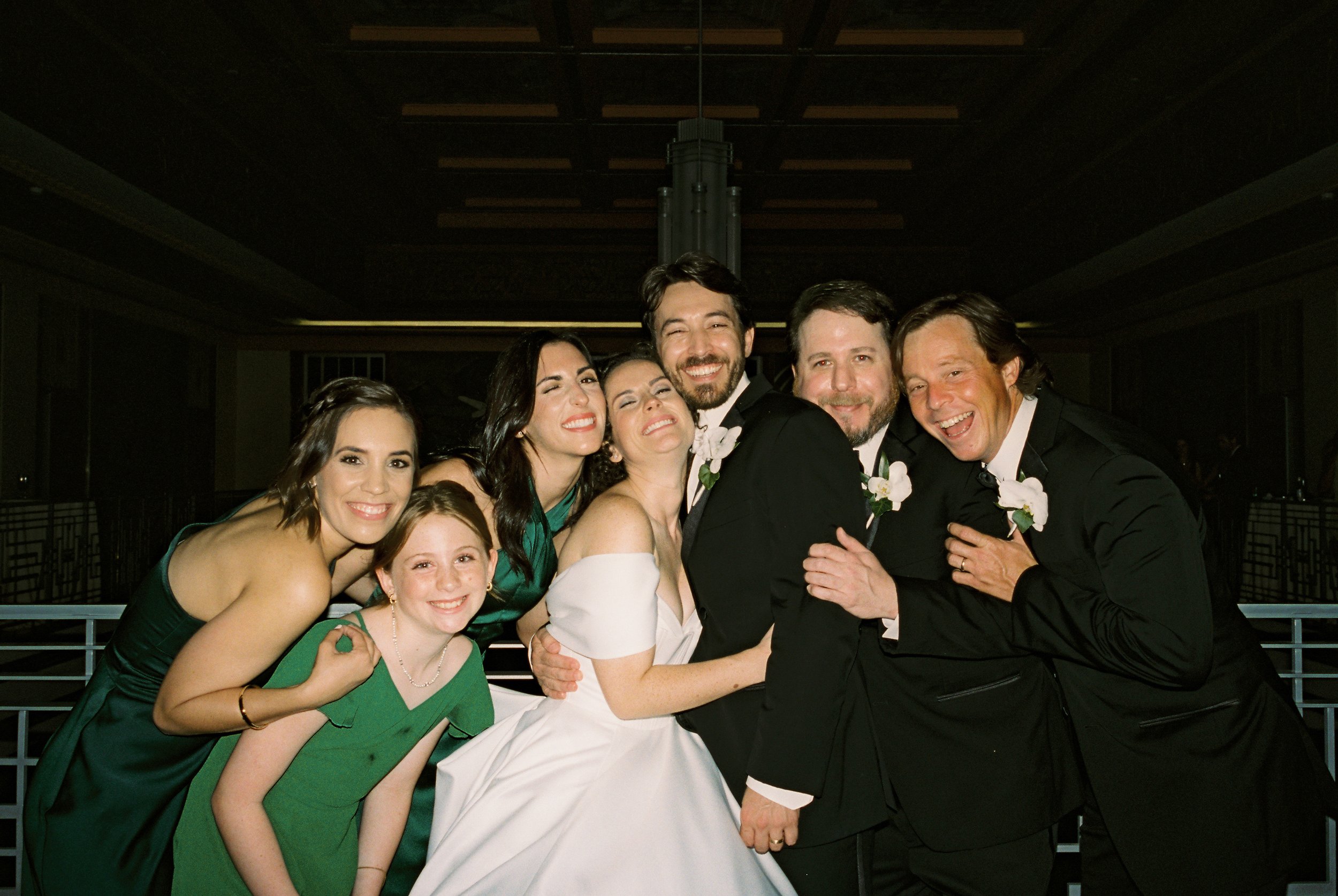 Wedding party gathers around the bride and groom for a joyful late-night portrait, showcasing documentary wedding photography moments.