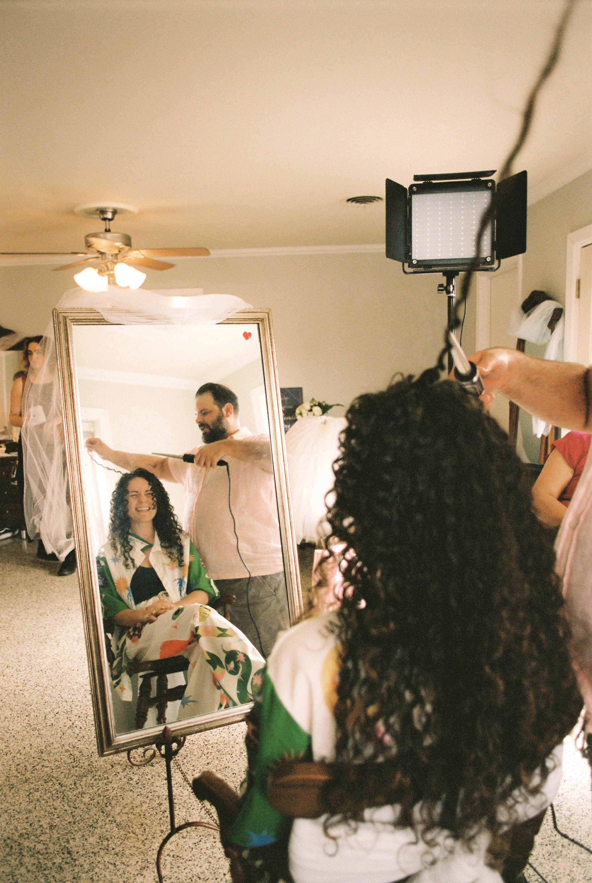 Bride gets her hair styled while reflected in a mirror during wedding morning preparations.