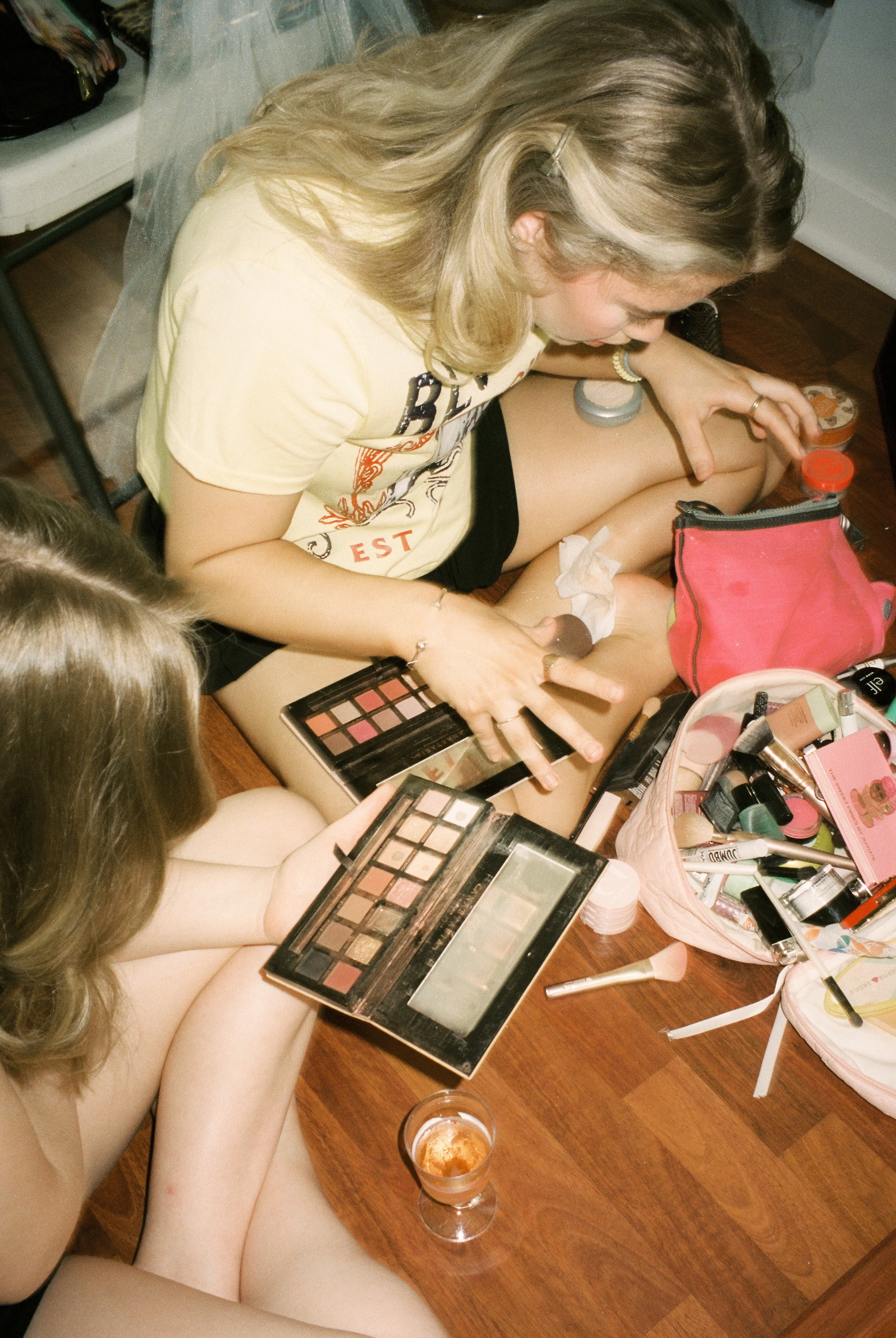 Wedding guest applies makeup while sitting on the floor surrounded by beauty products and getting-ready essentials.