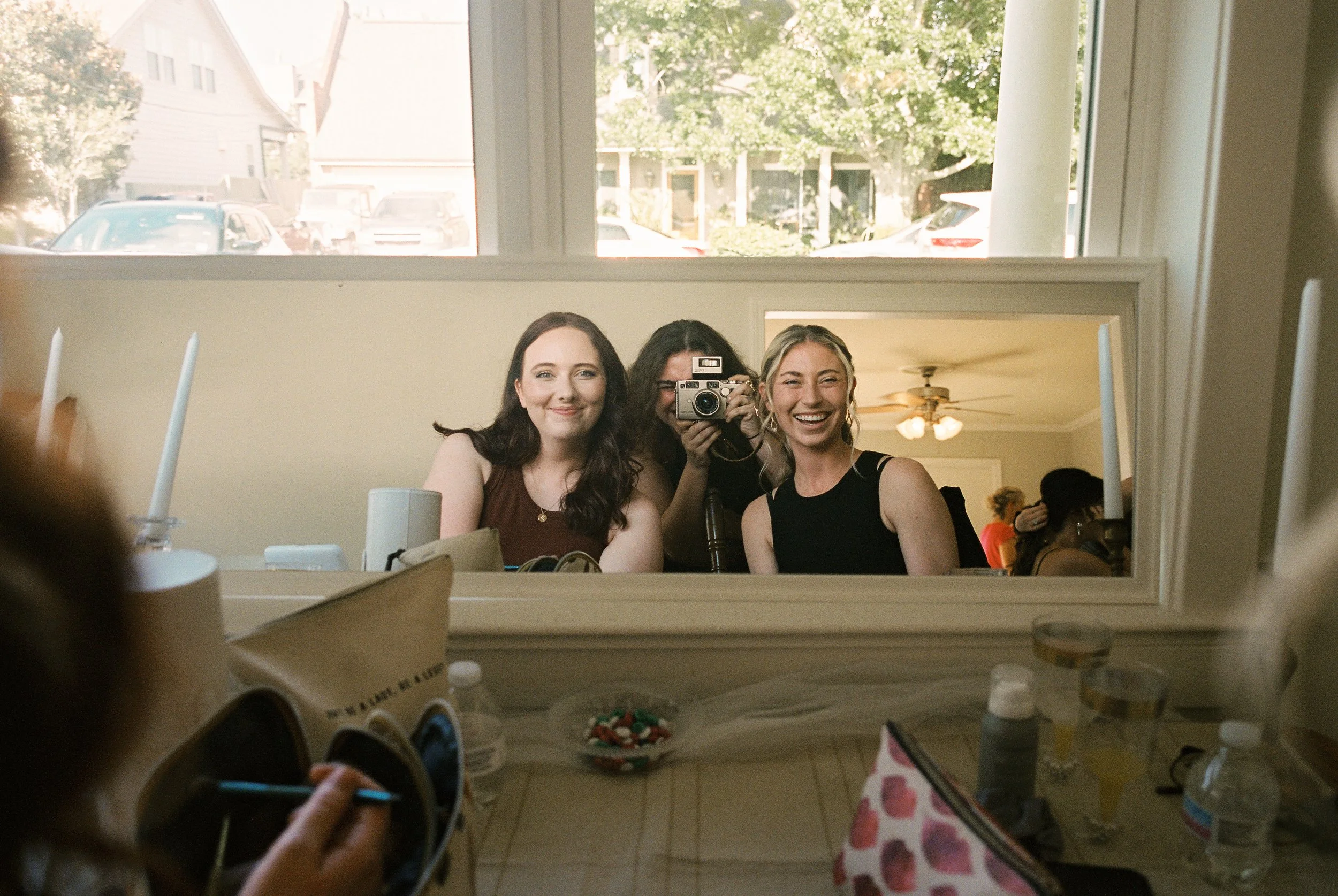 Bridesmaids smile in a mirror selfie while getting ready together before the wedding ceremony.