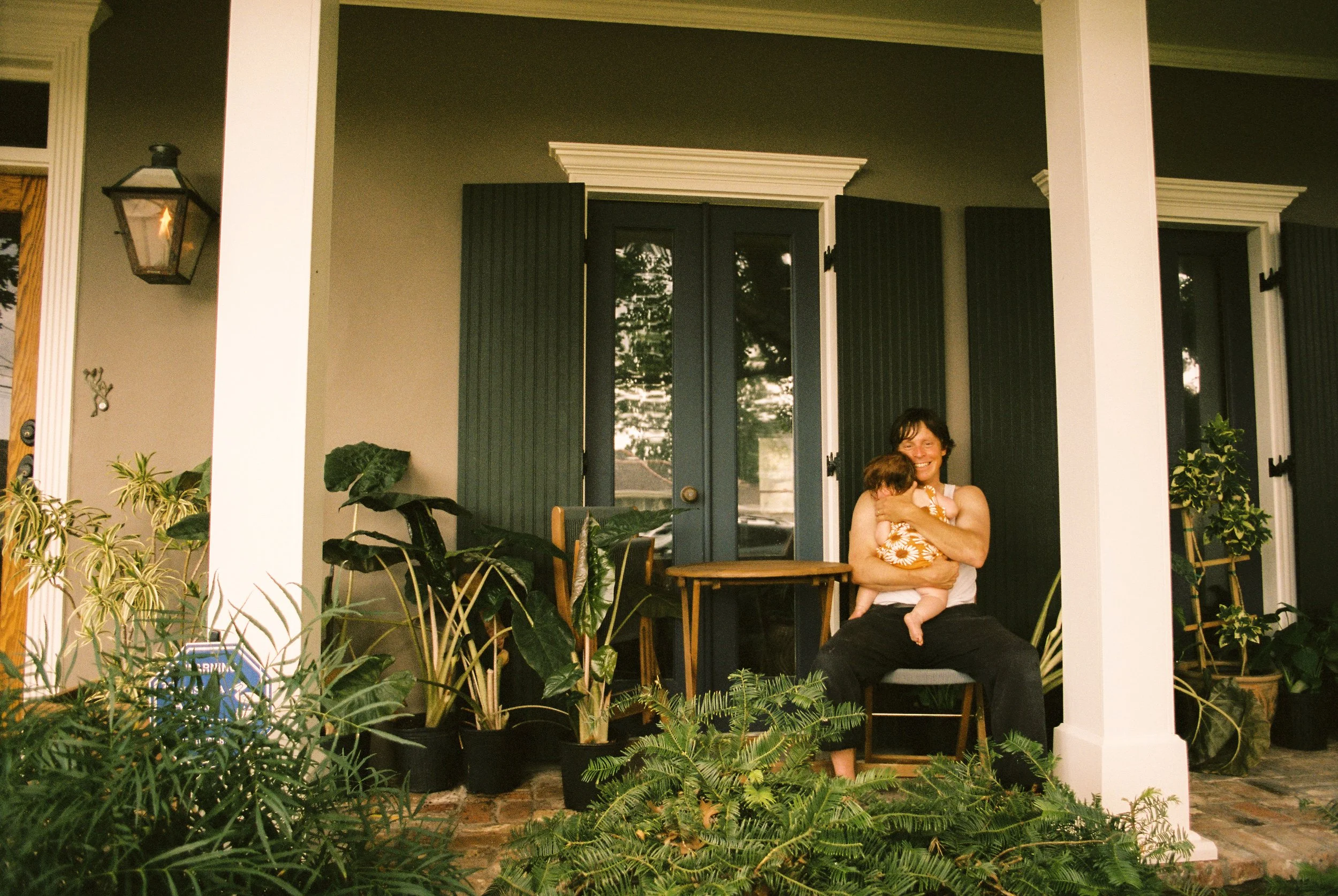 Groom relaxes on a front porch while holding a child before the wedding festivities begin.