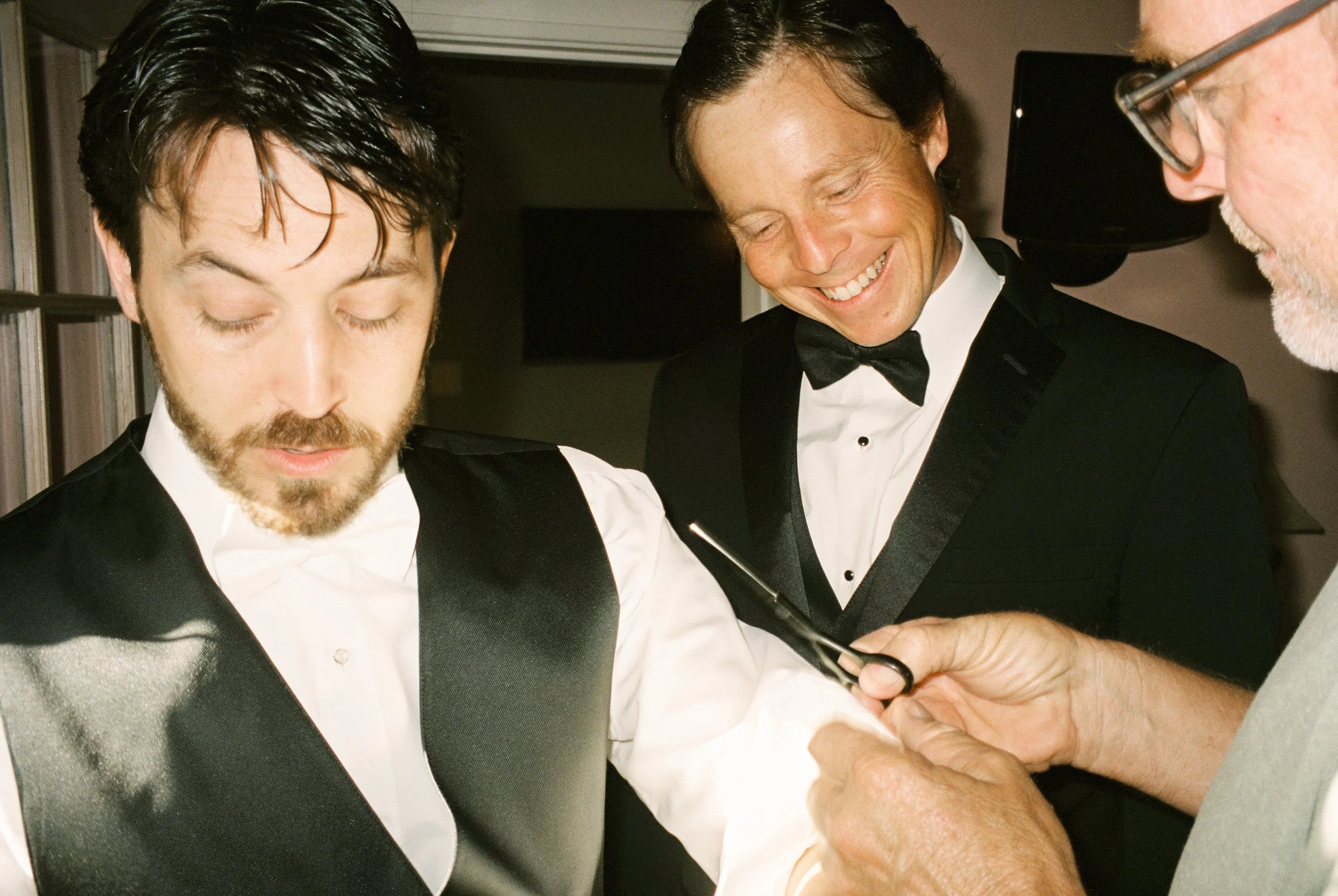 Groom prepares for the wedding as family members help adjust his formal attire, captured through documentary wedding photography.