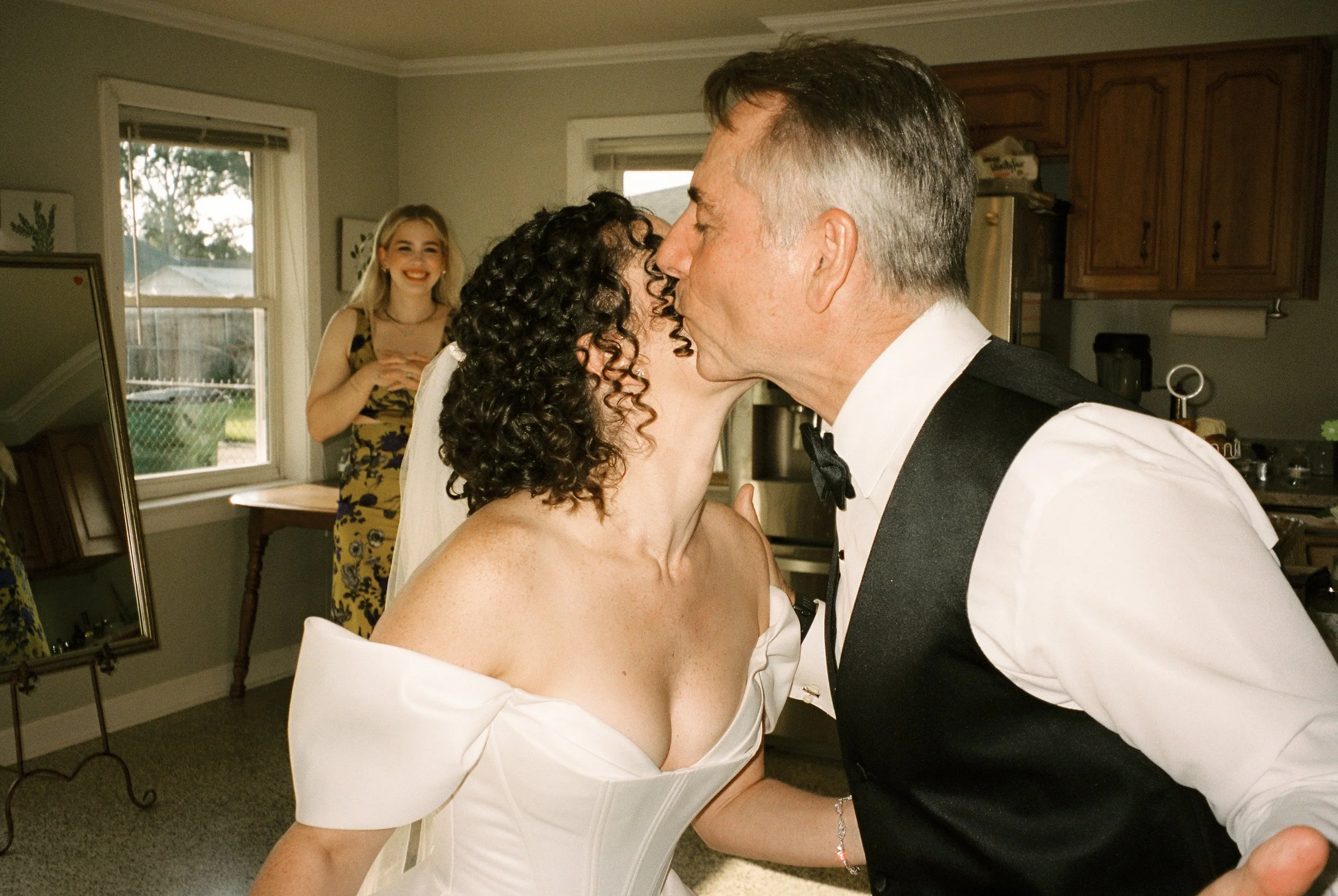 Bride shares an emotional kiss with a family member before the ceremony while loved ones look on.