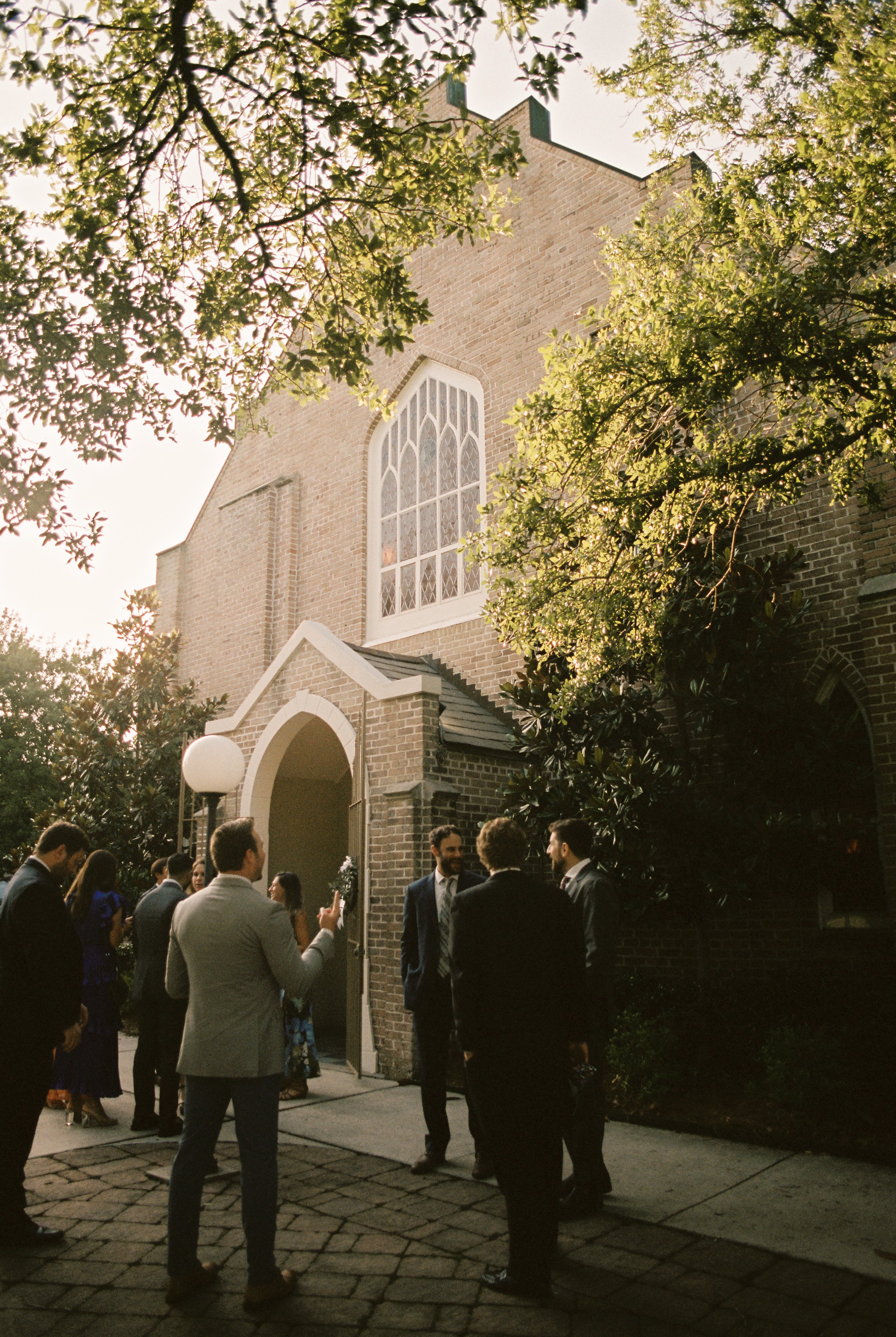 Wedding guests mingle outside a brick church before the ceremony begins, captured through documentary wedding photography.