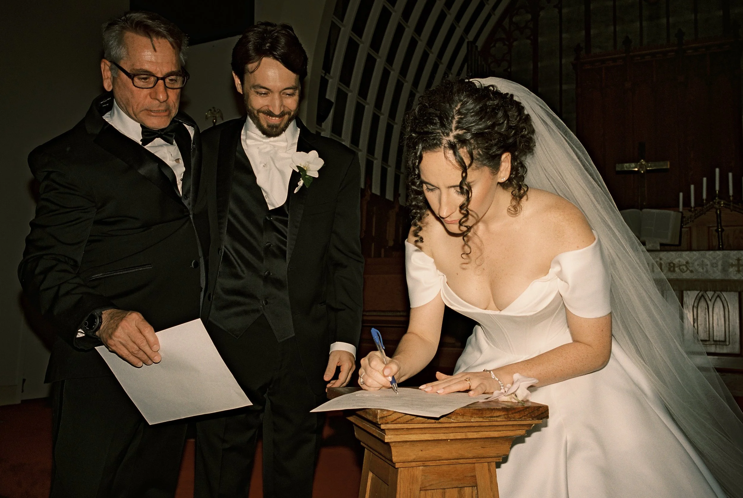 Bride signs the marriage license while the groom watches inside the church after the ceremony.