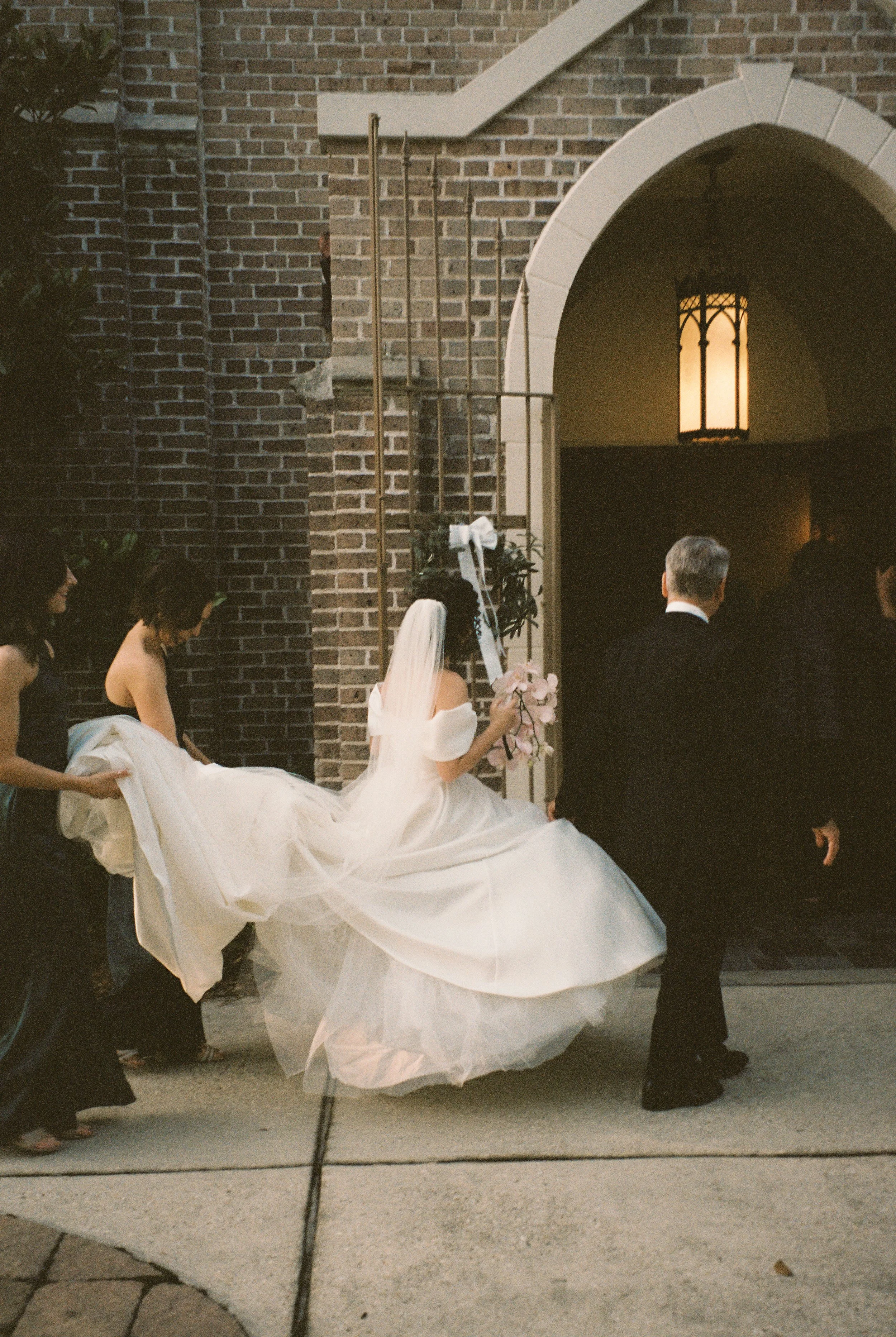 Bride arrives at the church entrance with attendants carrying her gown before the ceremony.