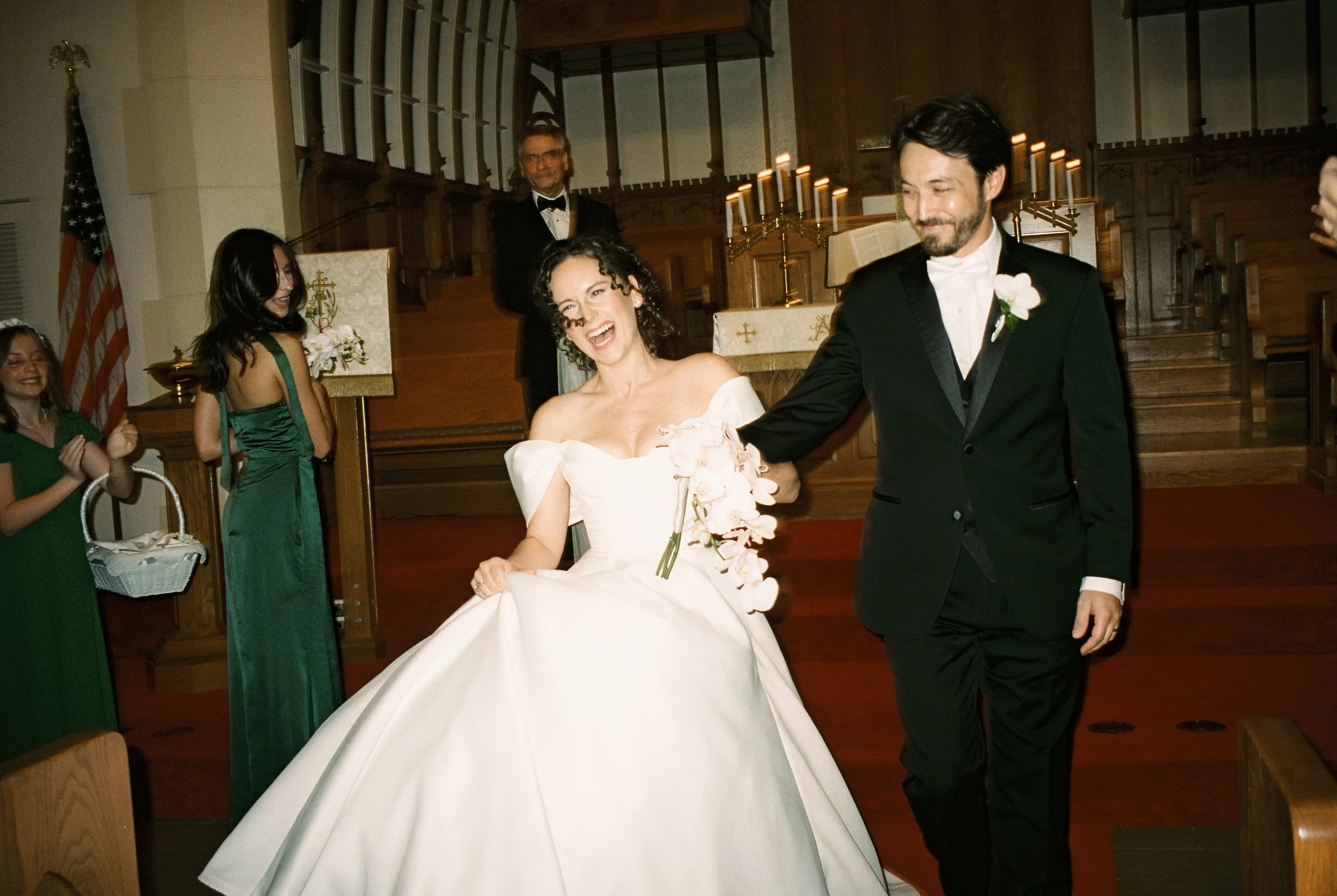 Newly married couple walks down the church aisle together after the ceremony, celebrating with smiles and laughter.