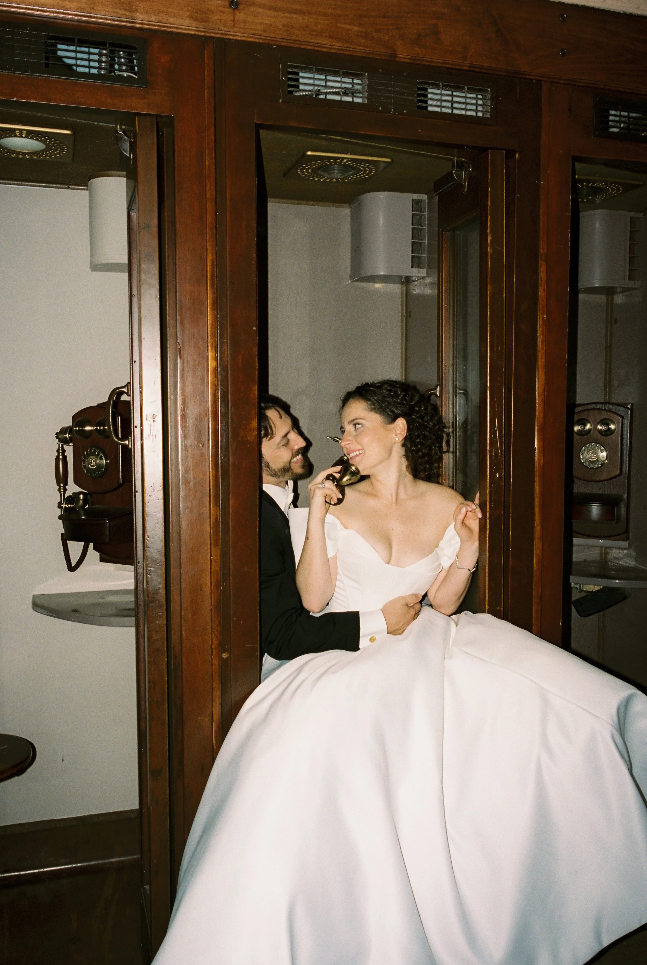 Bride and groom pose inside a vintage telephone booth, creating a playful and timeless wedding portrait.