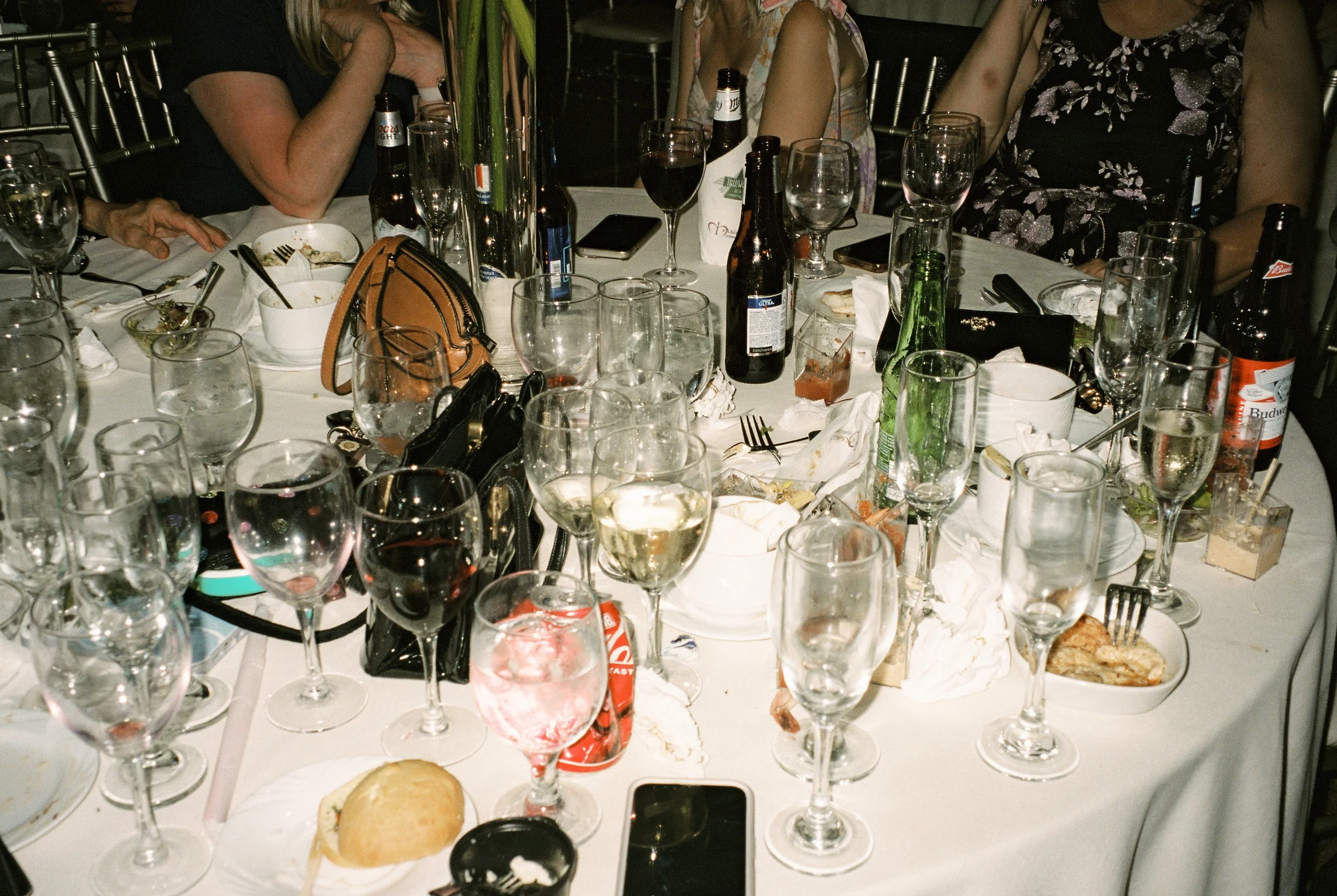 Reception table after dinner service, filled with glasses, bottles, plates, and candid signs of a lively gathering.