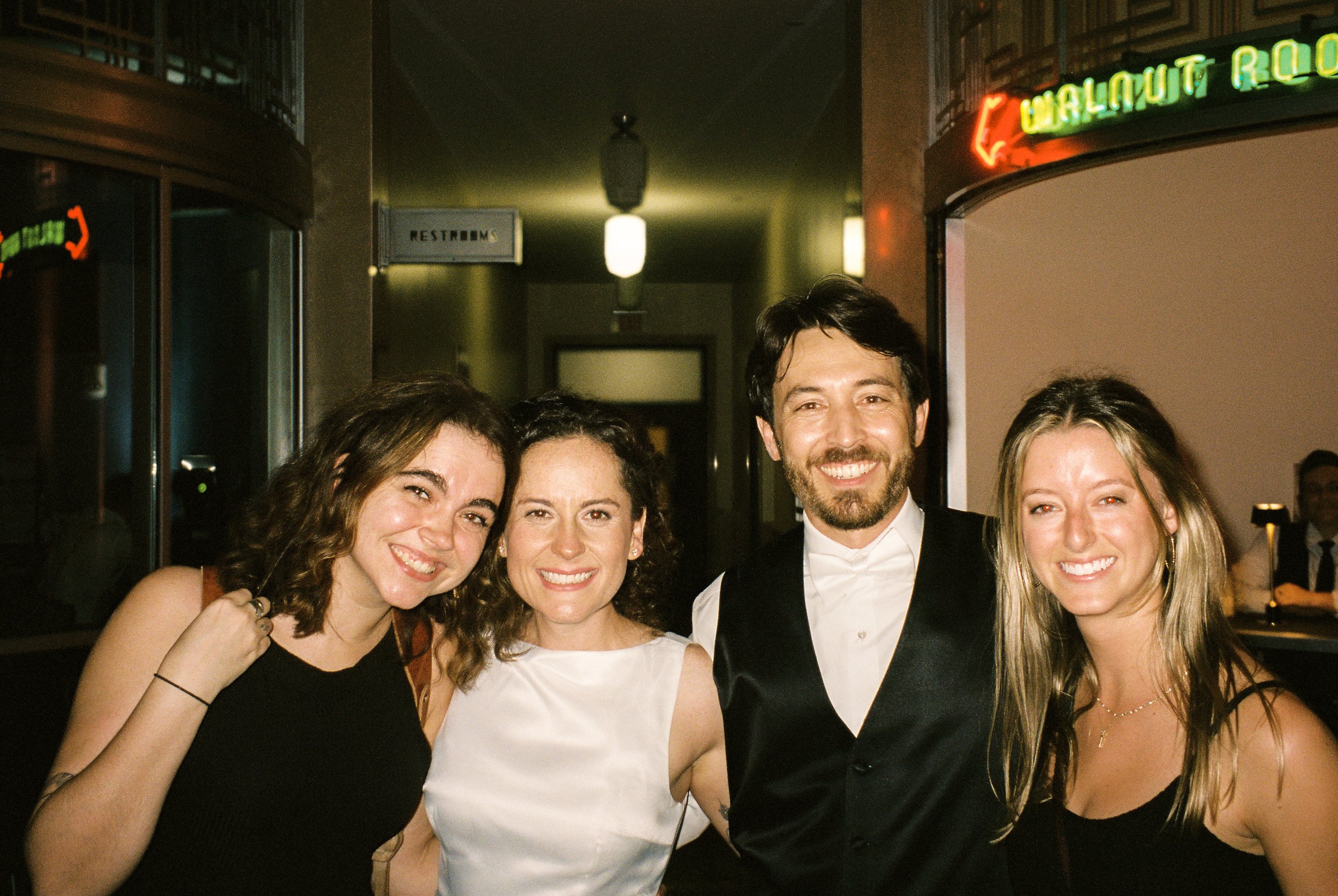 Newlyweds pose with friends for a casual group portrait at the reception venue.