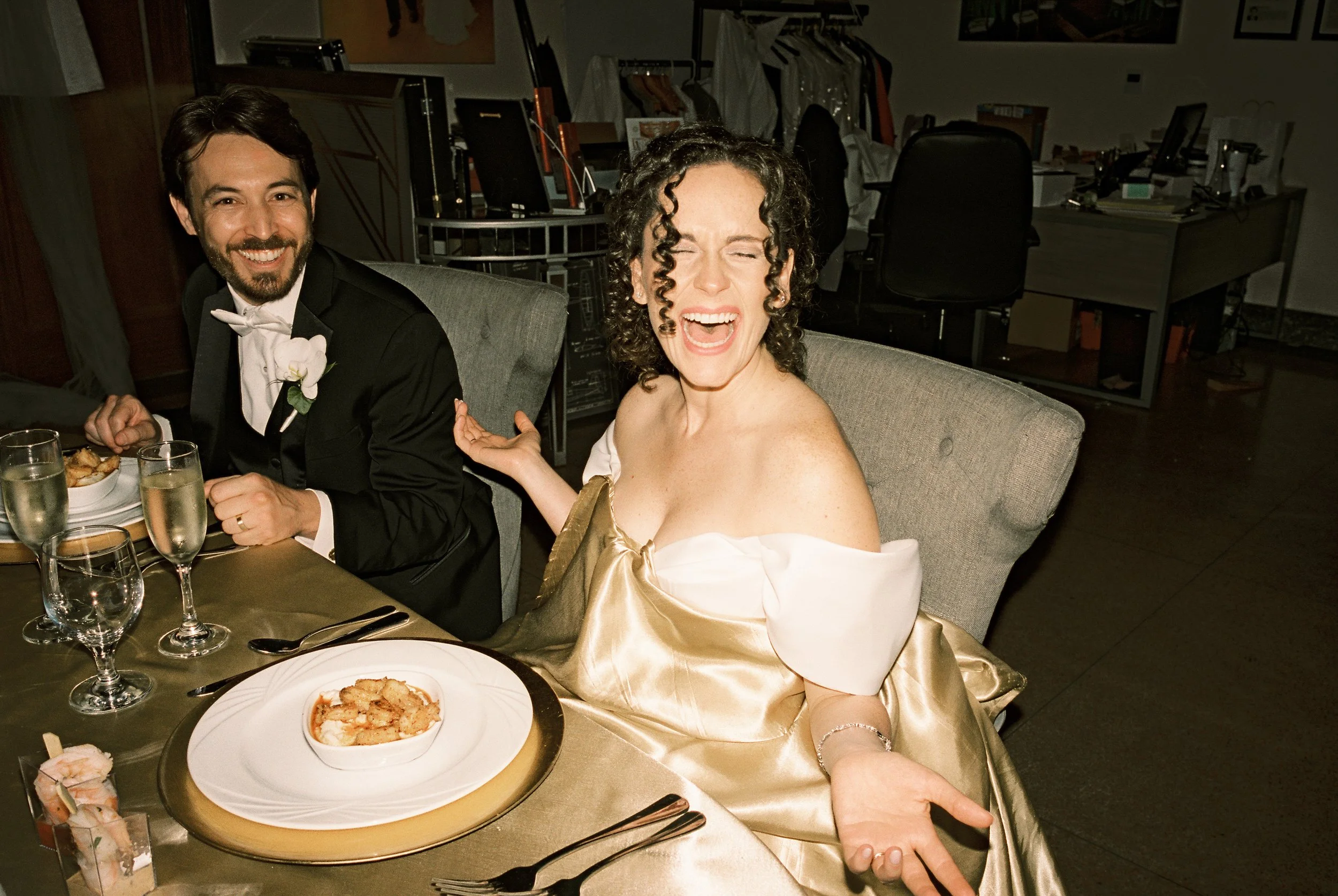Bride laughs at the reception table while dining with the groom in a candid wedding moment.