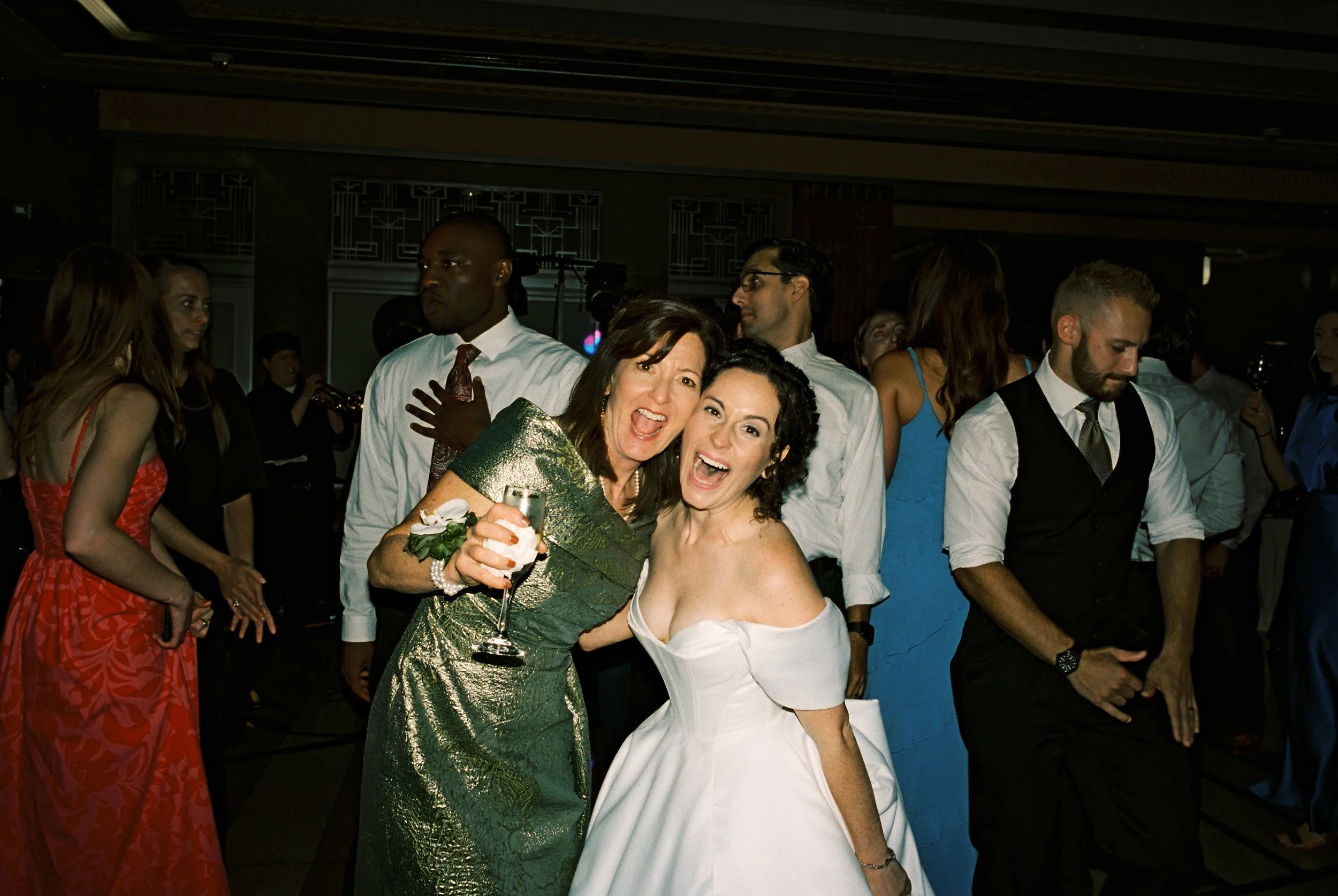 Bride dancing and posing with a guest in a shimmering green dress during the reception.