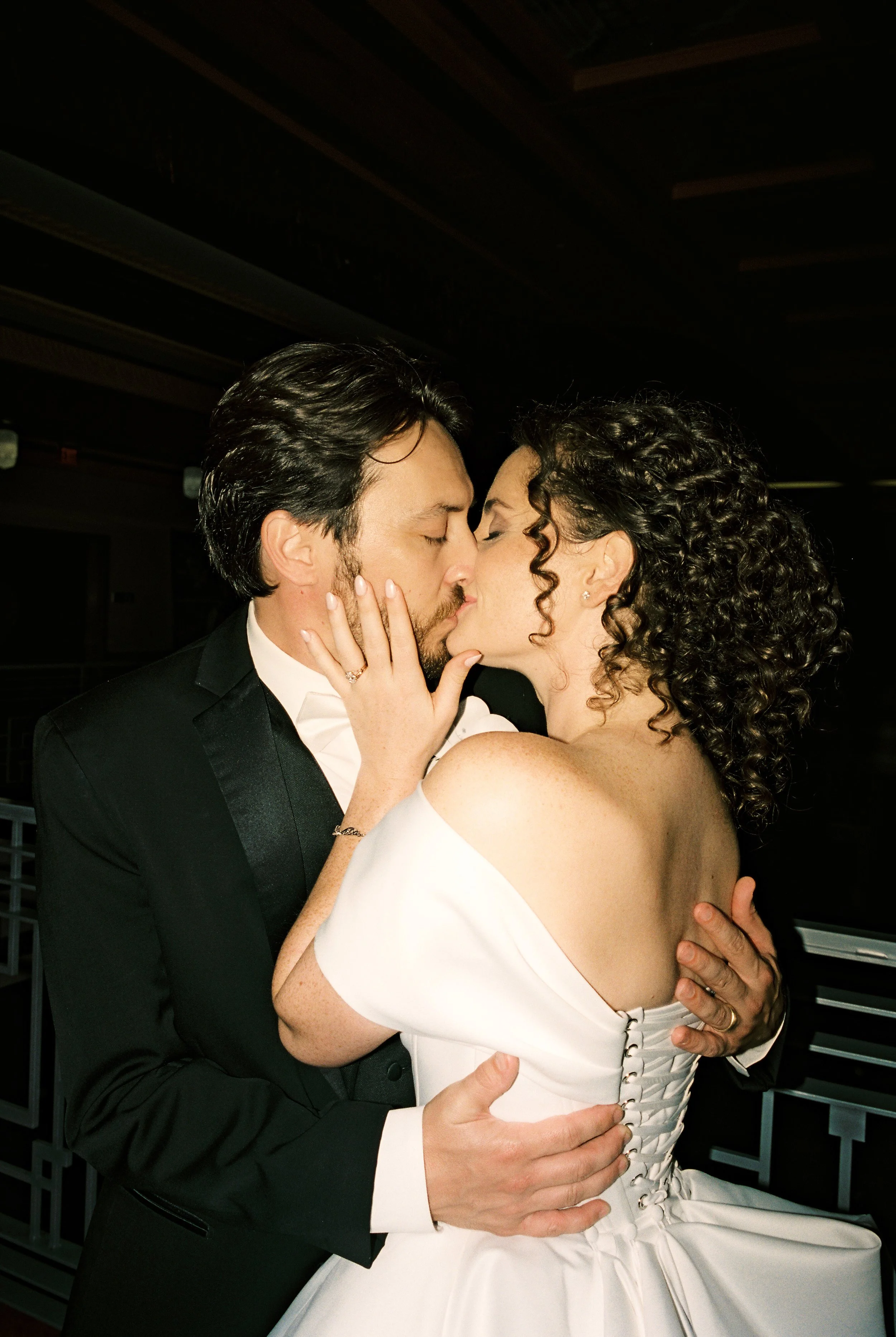 Close-up portrait of the bride and groom kissing, framed against the dark reception backdrop.