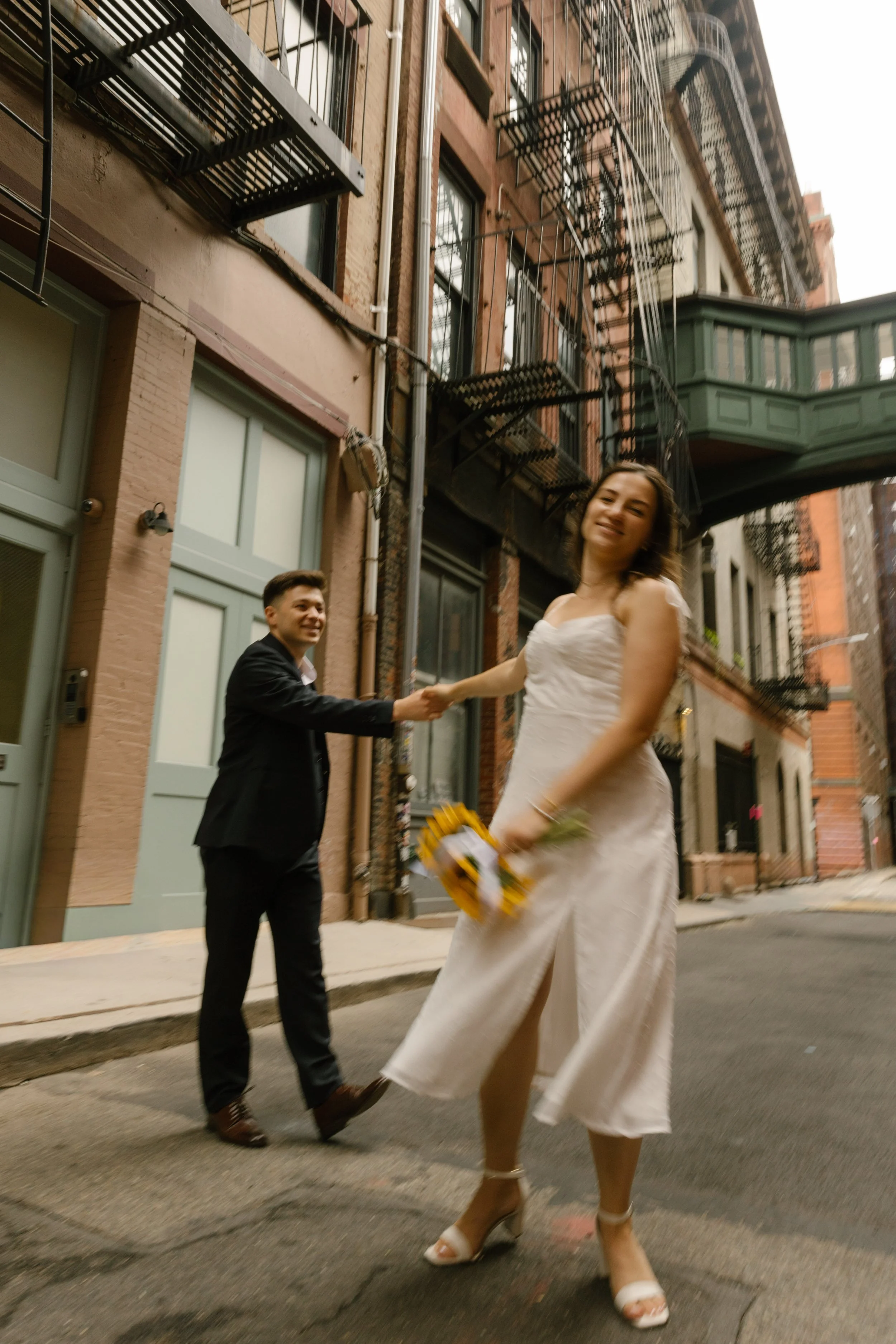 Bride twirling while holding her groom's hand on a charming New York City street, capturing the energy of Wedding Locations in NYC. 