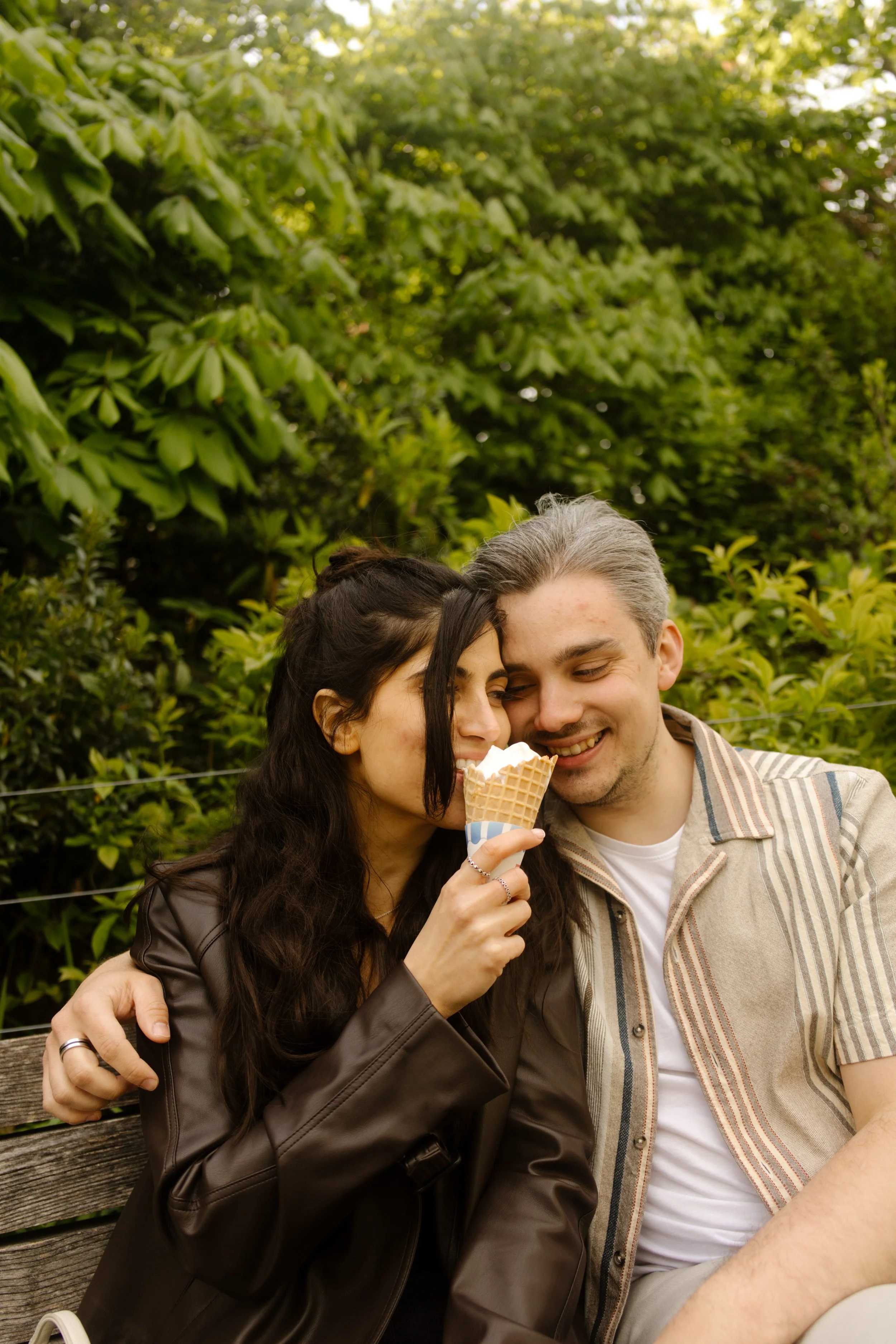 Couple shares an ice cream cone while cuddling on a park bench during a relaxed New York engagement session.