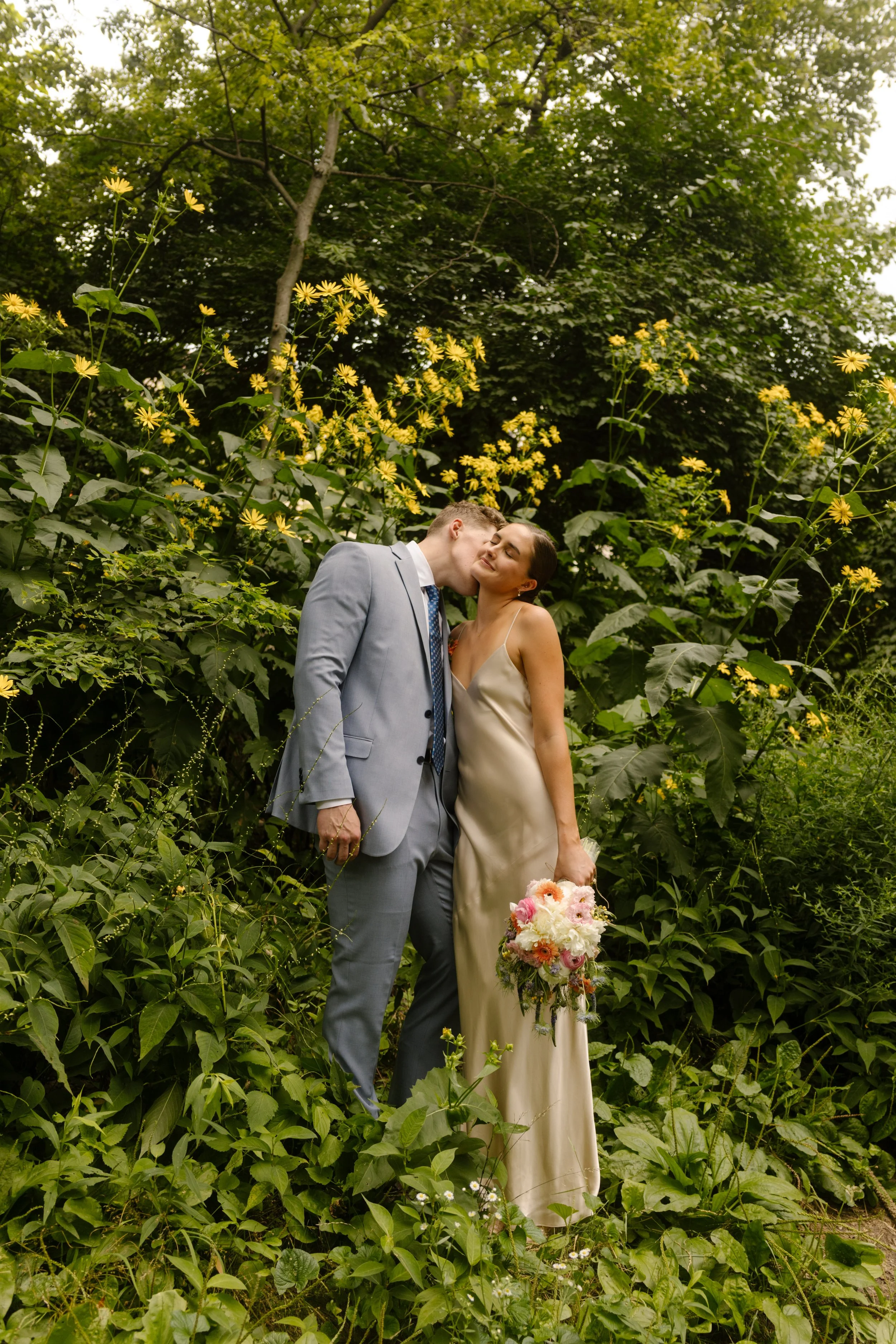 Romantic wedding portrait of a couple surrounded by lush greenery in Central Park during summer.