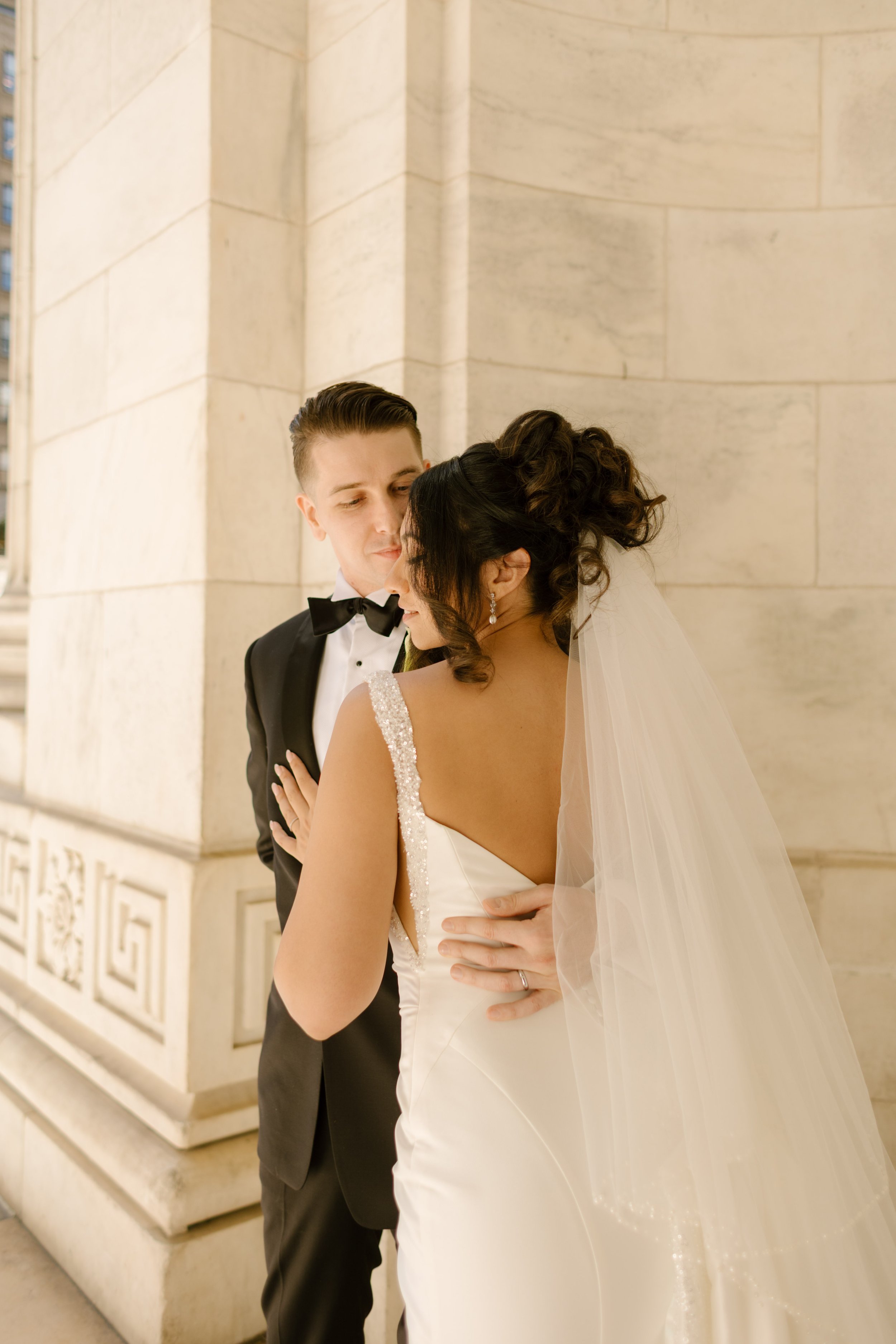 Bride and groom embrace beneath marble columns outside a classic New York wedding venue.