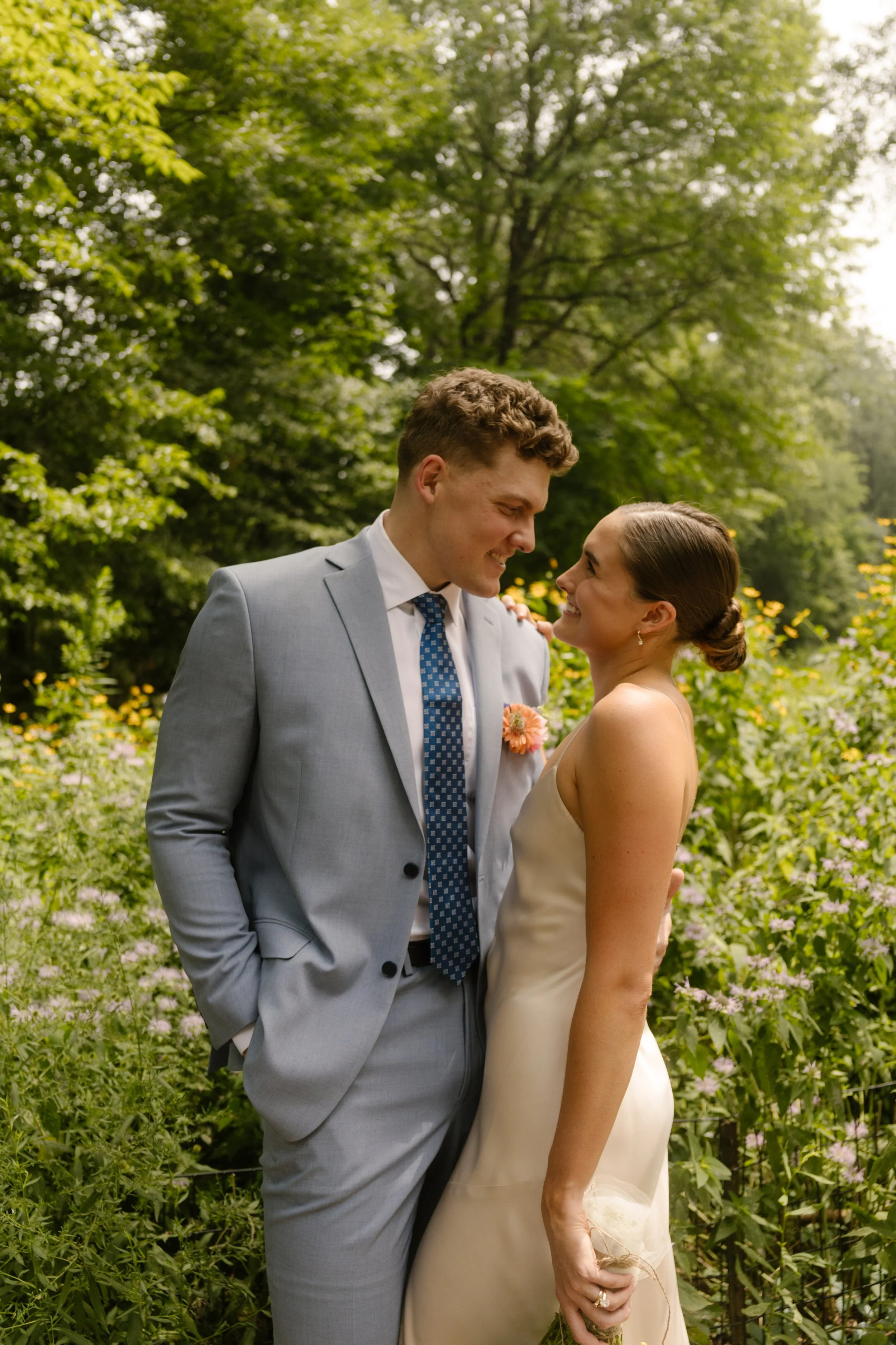 Newlyweds smile at each other surrounded by lush greenery in a peaceful city garden.