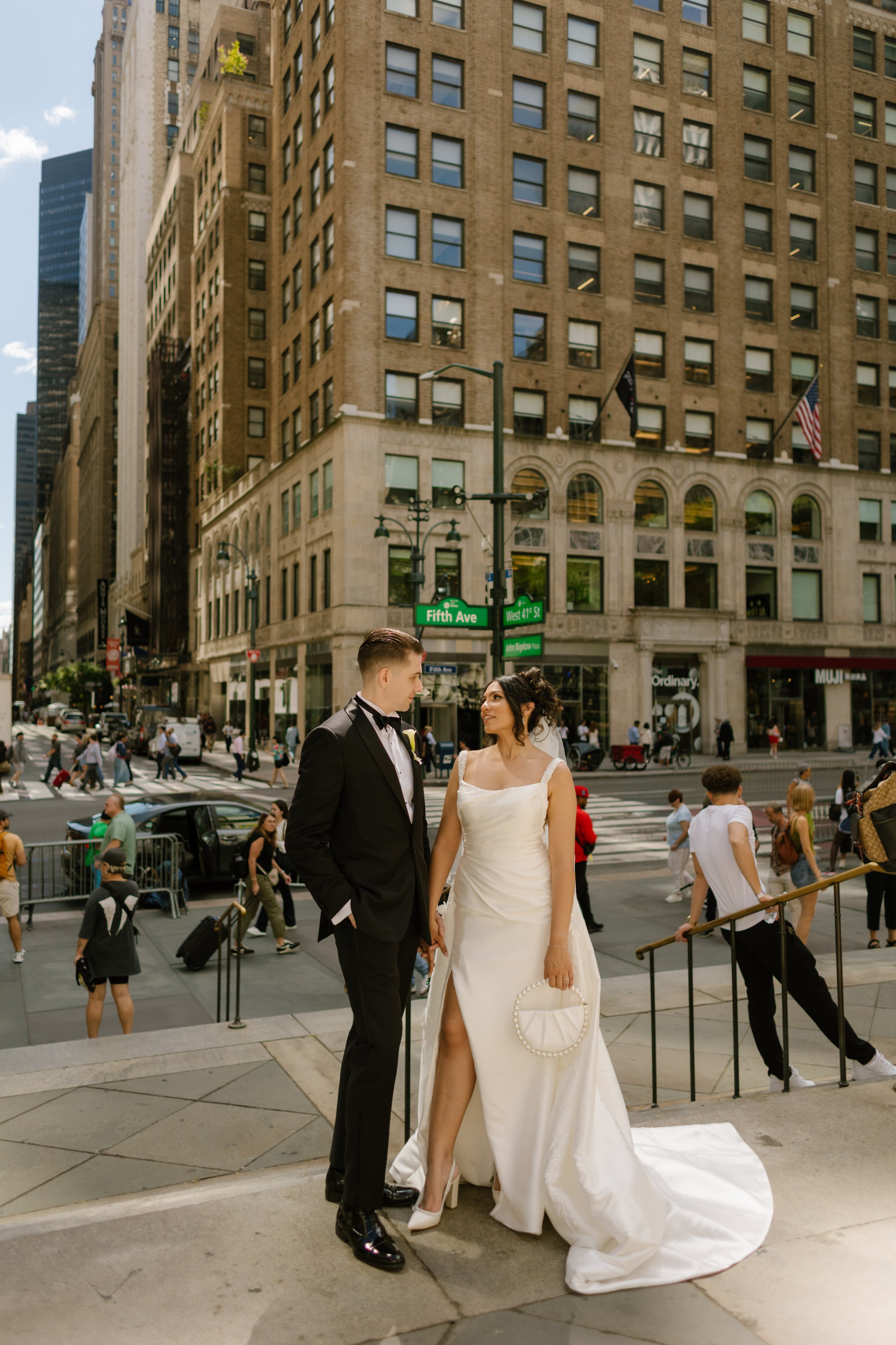 Bride and groom stand together on Fifth Avenue surrounded by iconic Manhattan architecture and city streets.