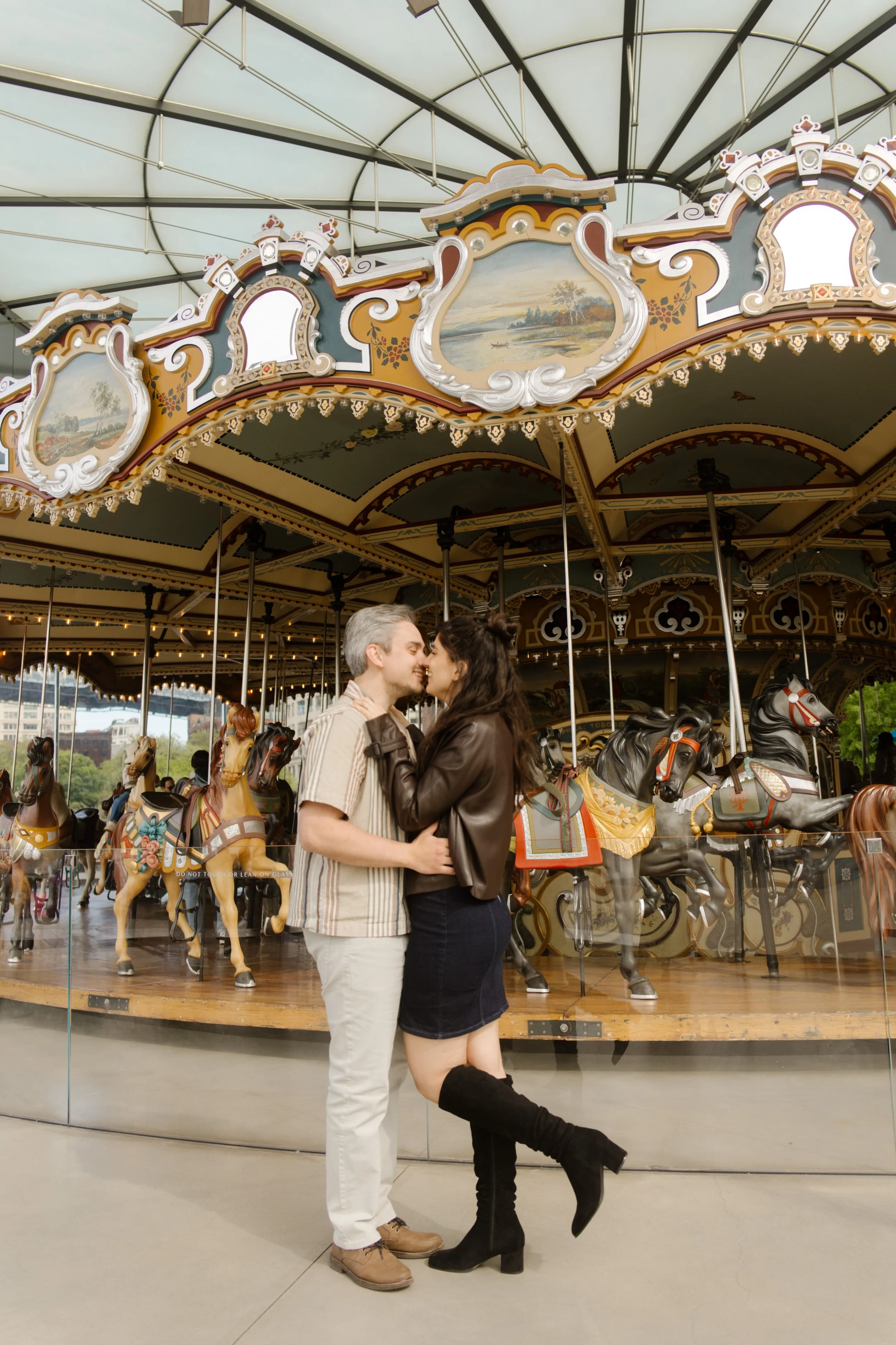 Couple kisses in front of Jane's Carousel in Brooklyn Bridge Park, showcasing playful Wedding Locations in NYC.