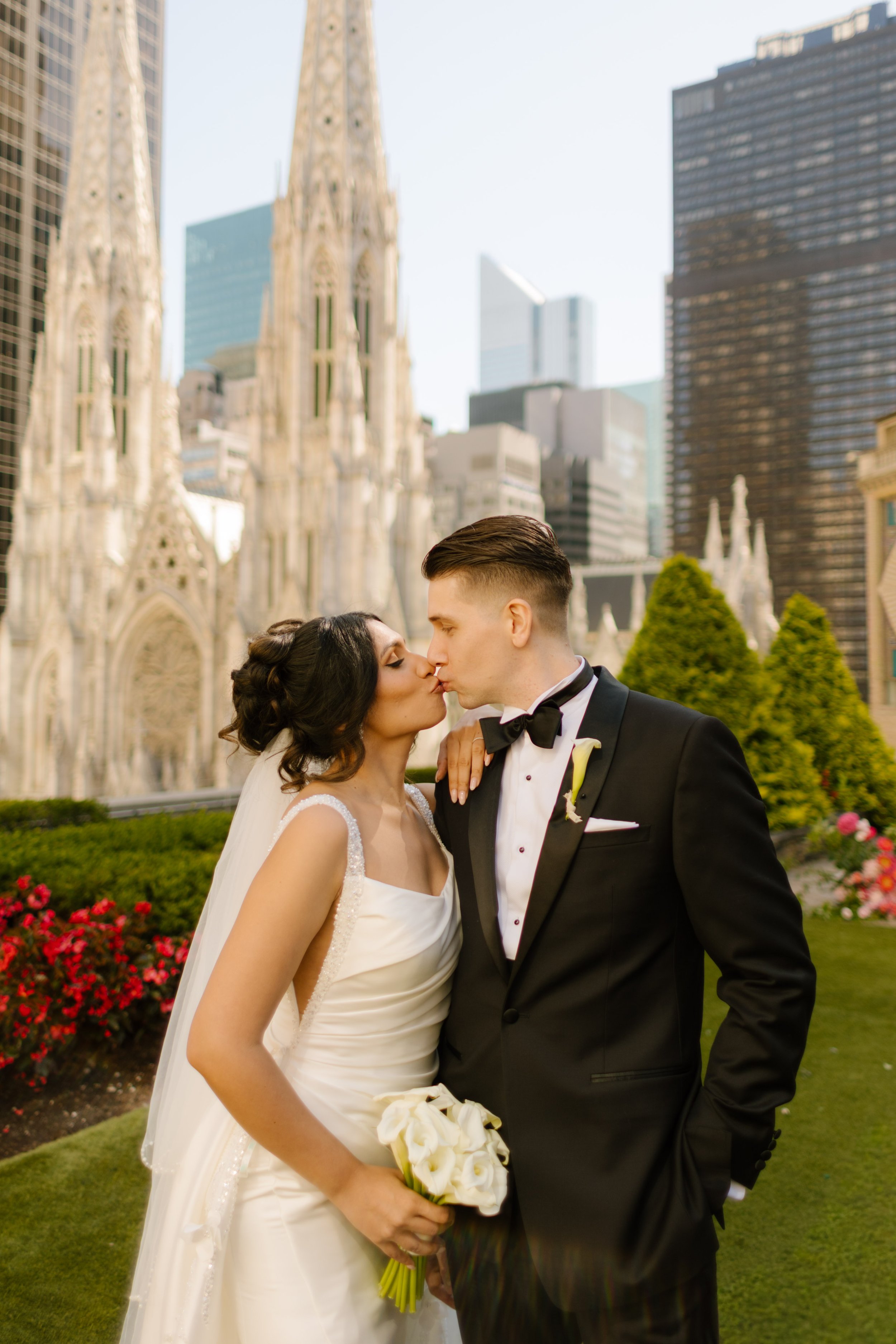 Bride and groom kiss on a rooftop terrace with St. Patrick's Cathedral and the Manhattan skyline, featuring elegant Wedding Locations in NYC.
