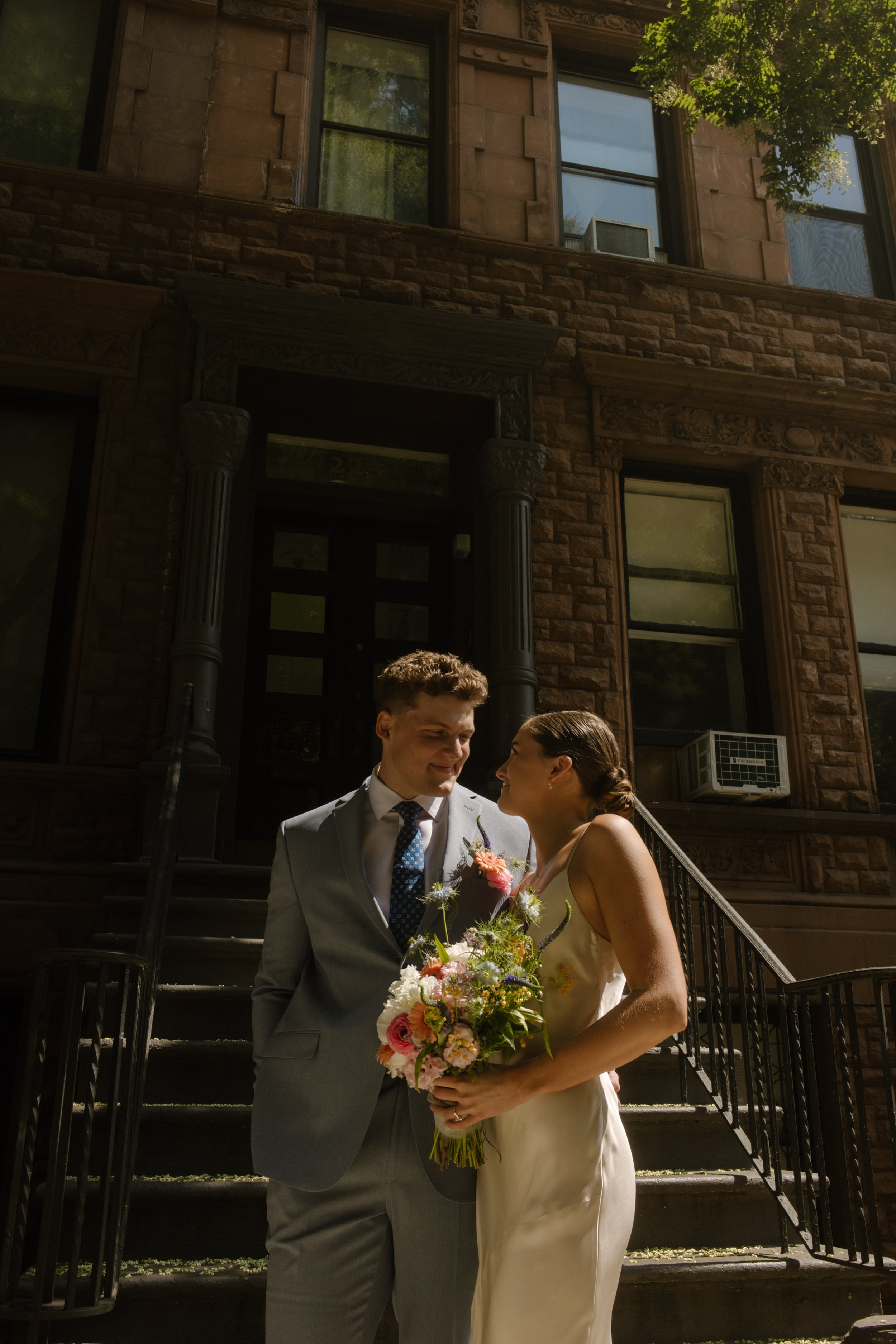 Bride and groom share a quiet moment on the steps of a historic brownstone, highlighting charming Wedding Locations in NYC.
