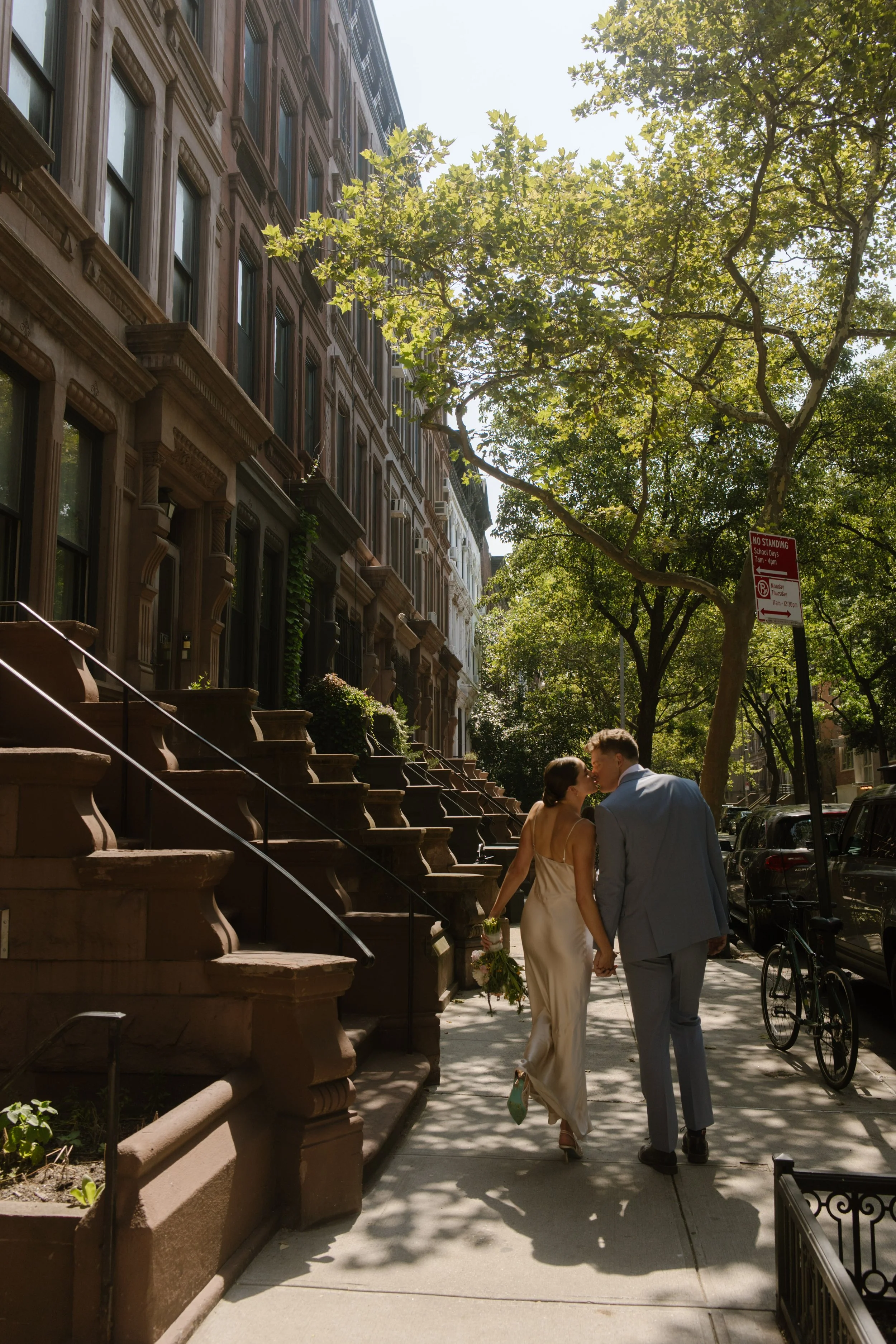 Newlyweds walk hand in hand along a tree-lined Brooklyn brownstone street after their intimate wedding.