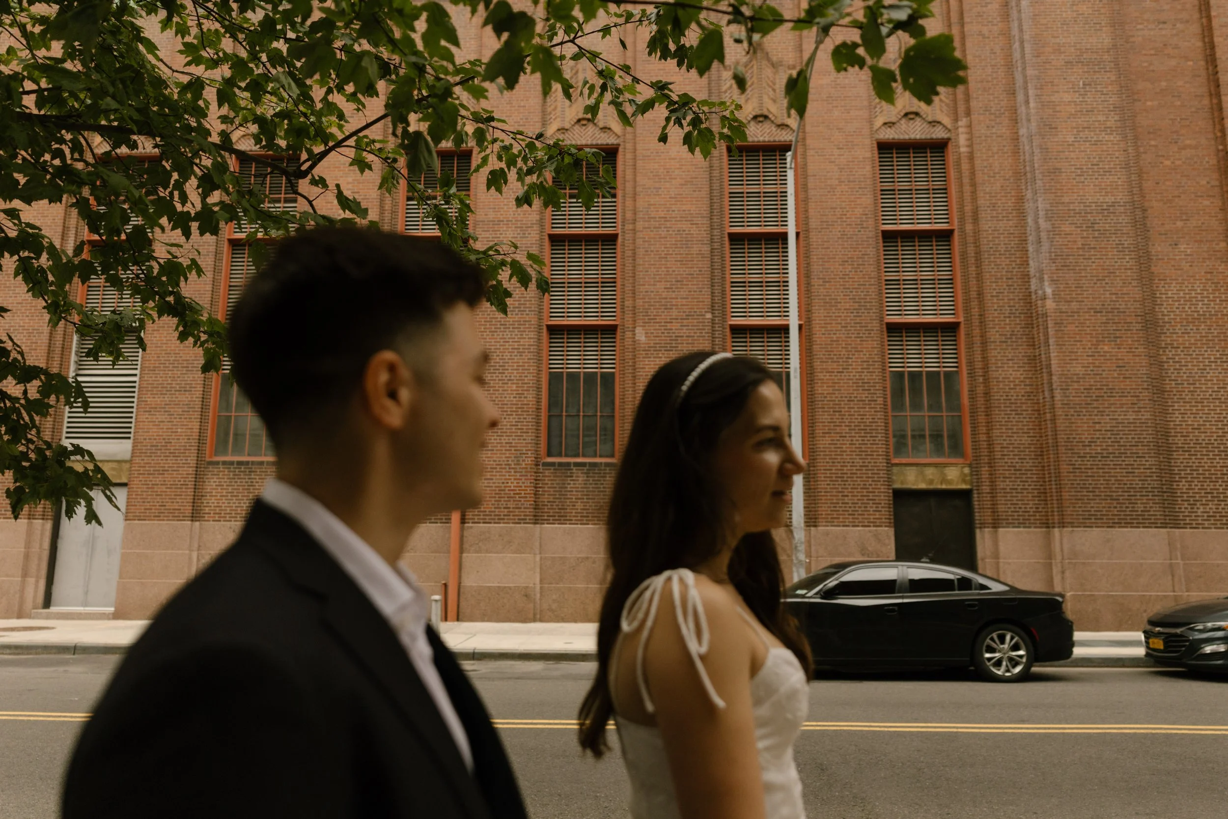 Newlyweds stroll together through a quiet Manhattan street lined with historic brick architecture.