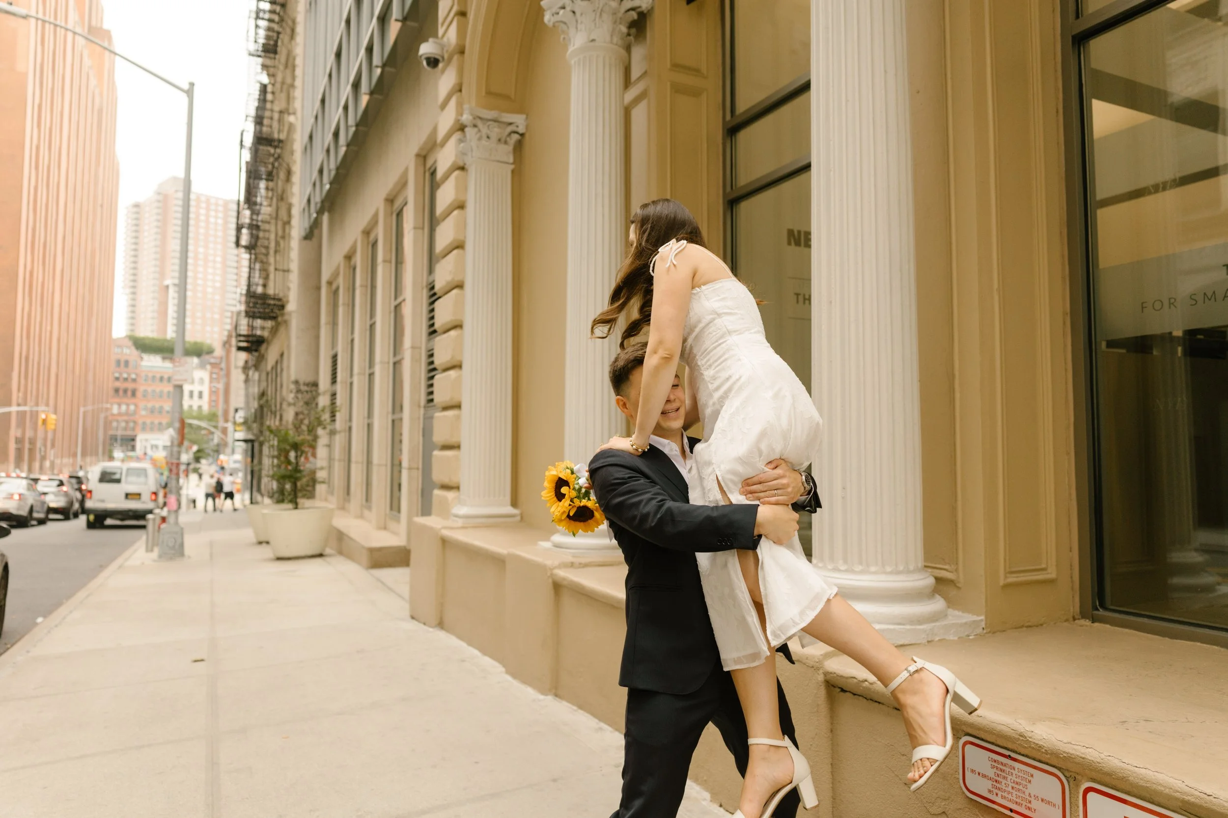 Groom lifts the bride onto a ledge outside a classic SoHo building for a fun New York wedding portrait.