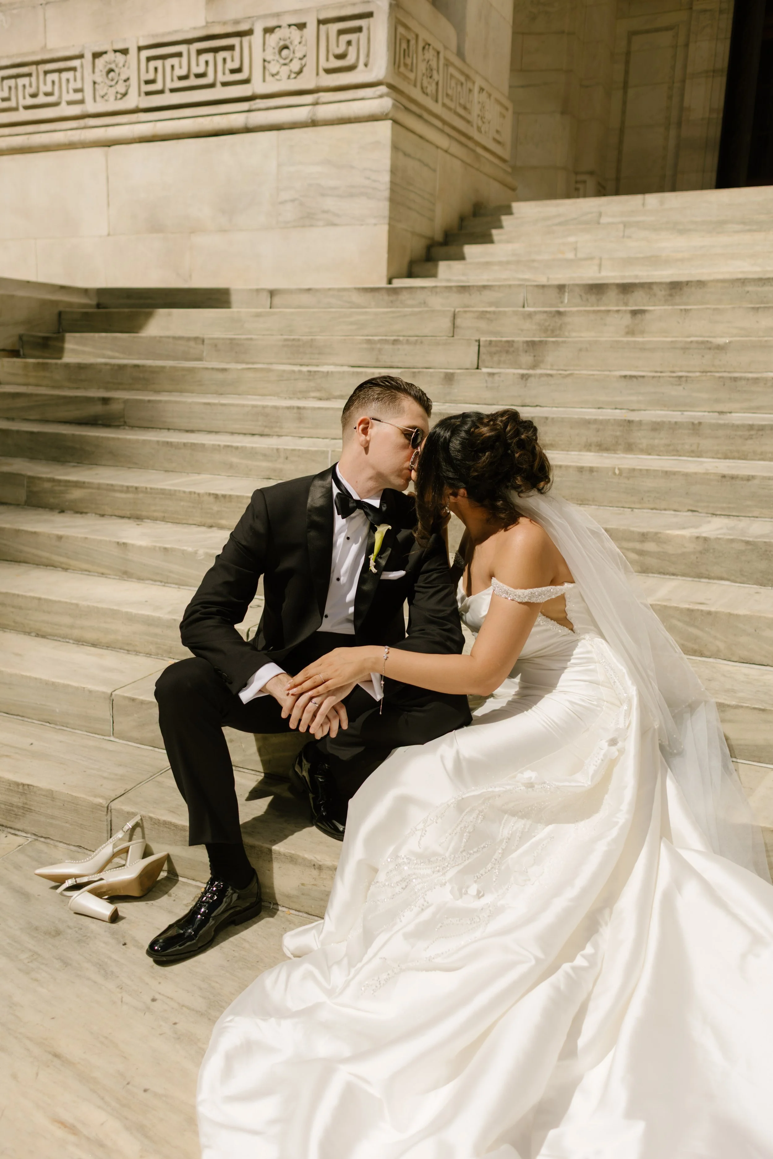 Bride and groom share a quiet moment on marble steps outside a historic New York landmark.