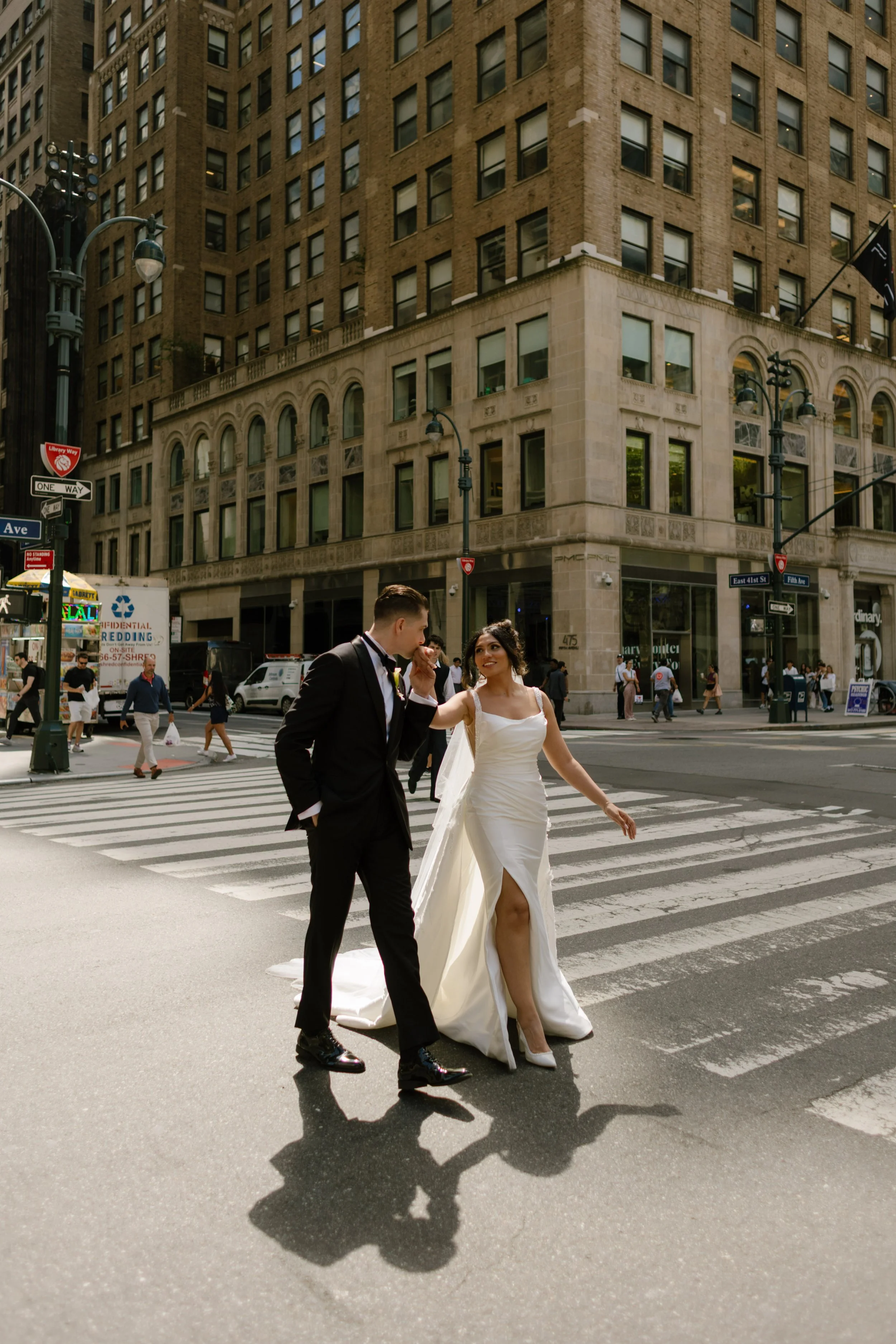 Bride and groom cross a Manhattan intersection hand in hand surrounded by classic New York City architecture.