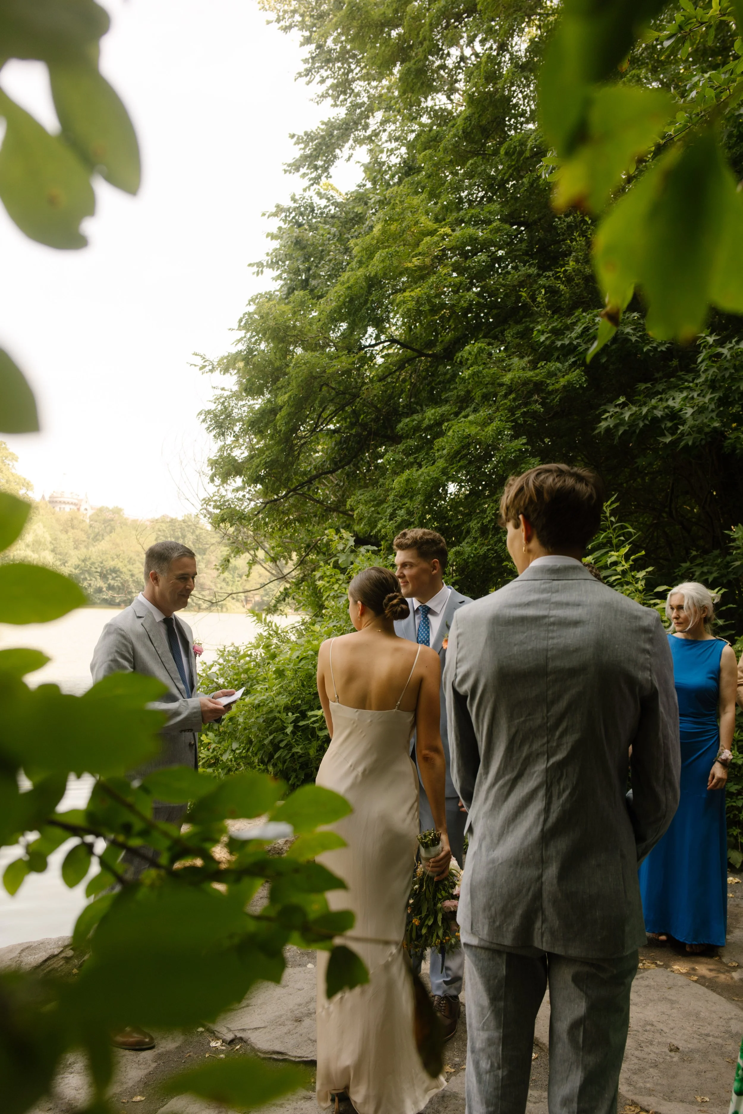 Intimate Central Park wedding ceremony beside the lake with family gathered beneath the trees at one of the most scenic Wedding Locations in NYC.