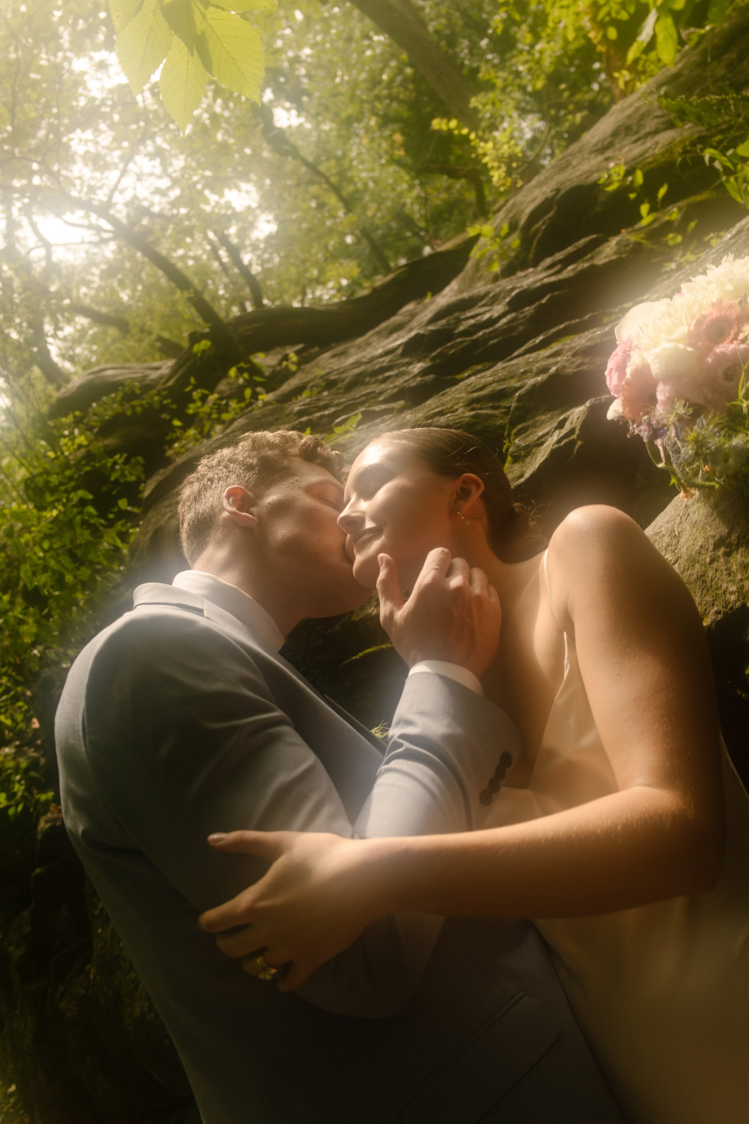 Romantic close-up of newlyweds sharing a kiss among sunlit rock formations in Central Park, highlighting Wedding Locations in NYC.