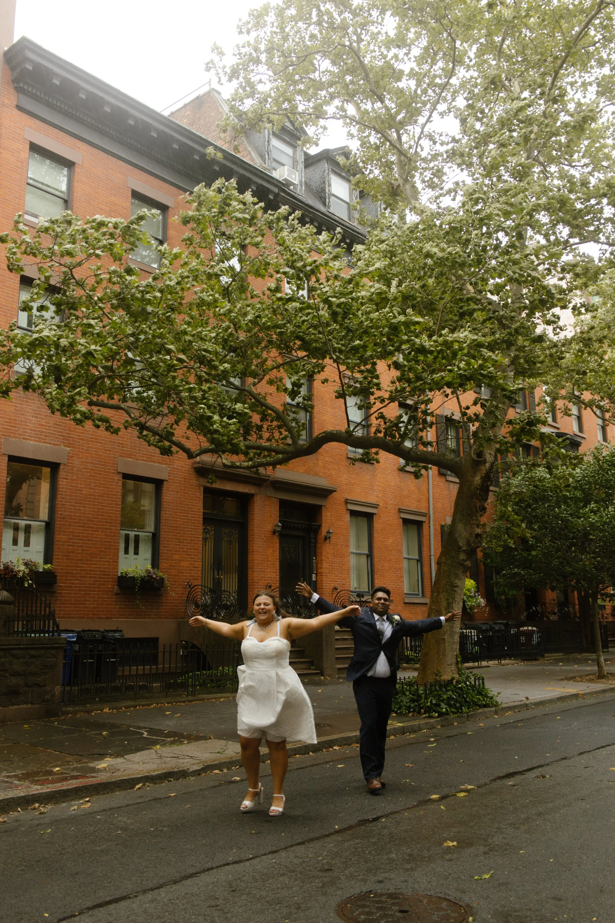 Newlyweds celebrate with arms outstretched on a historic brownstone street after their New York City wedding.