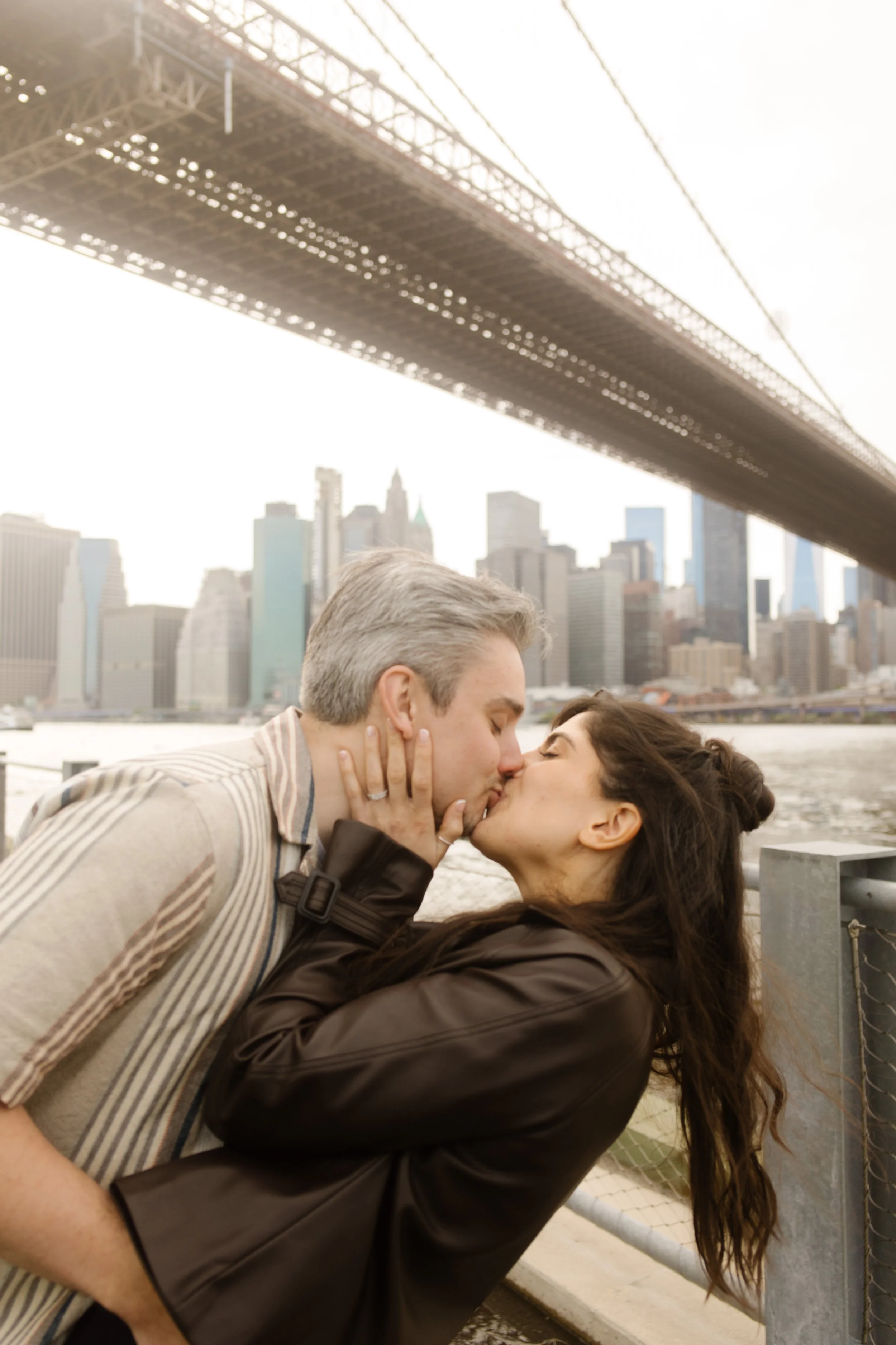 Couple shares a kiss beneath the Brooklyn Bridge with the Manhattan skyline behind them, one of the most recognizable Wedding Locations in NYC.