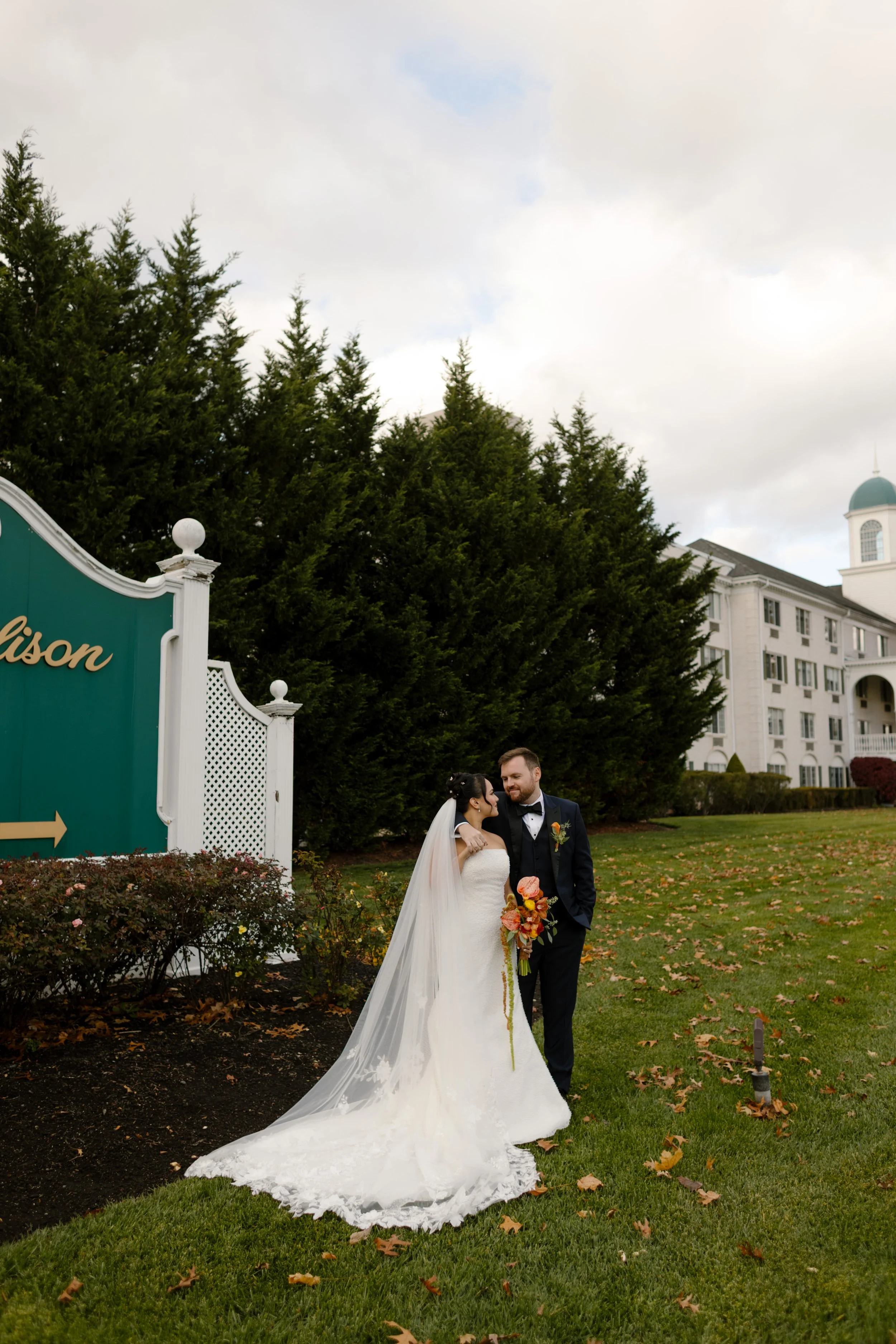 Newlyweds walk across the lawn outside The Madison Hotel with vibrant fall florals after their wedding celebration.