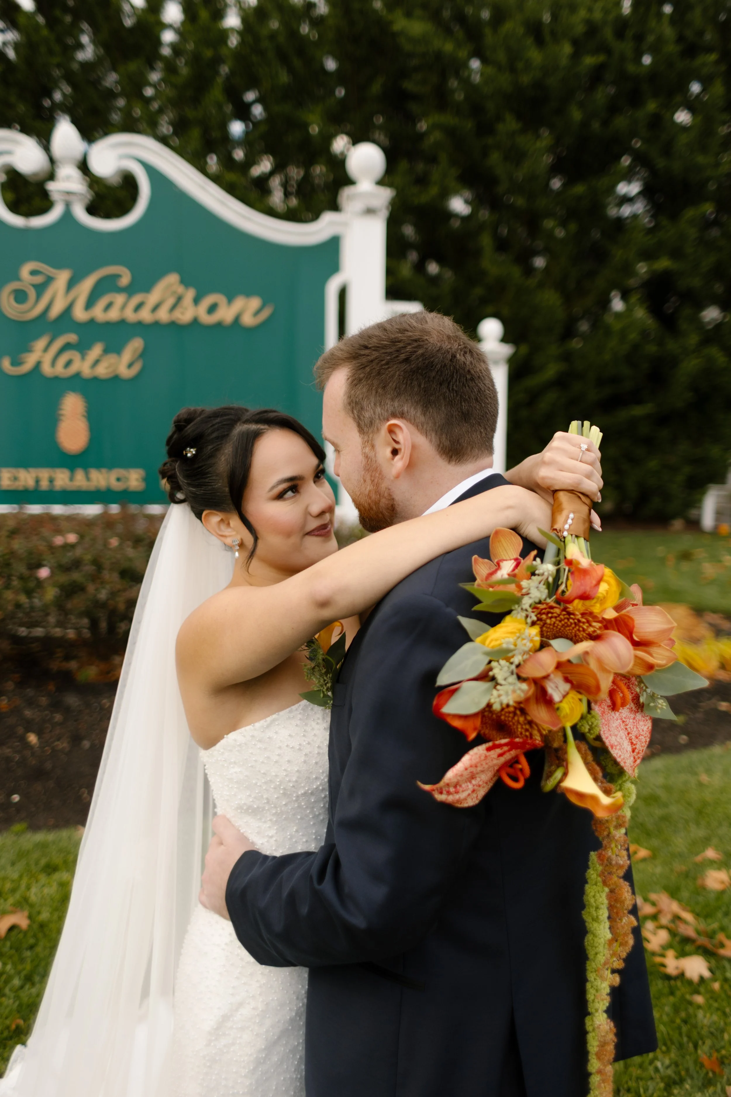 Bride and groom laugh together on the lawn outside The Madison Hotel surrounded by fall foliage and elegant grounds.