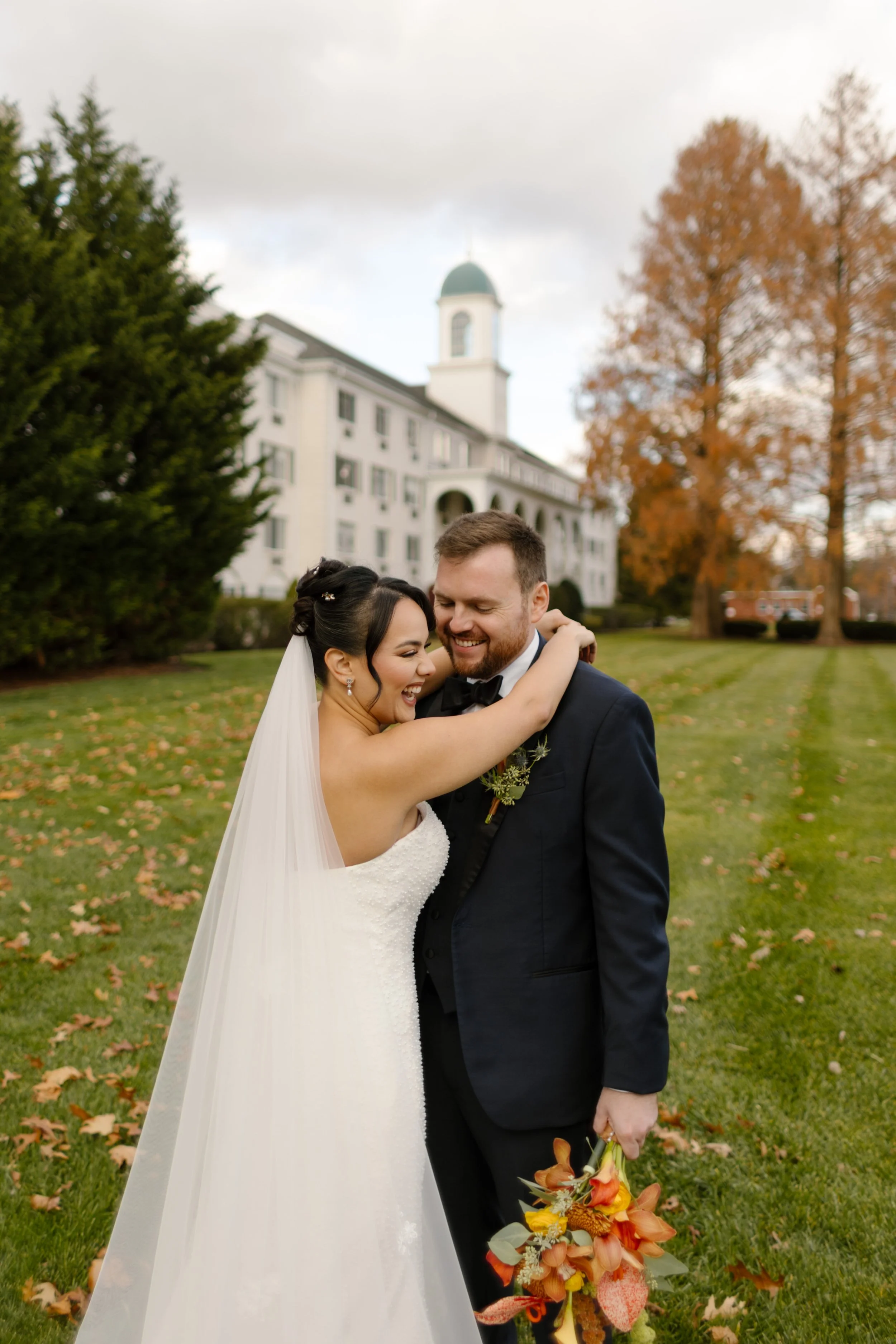 Bride hugs her groom while holding a colorful autumn bouquet in front of The Madison Hotel entrance.