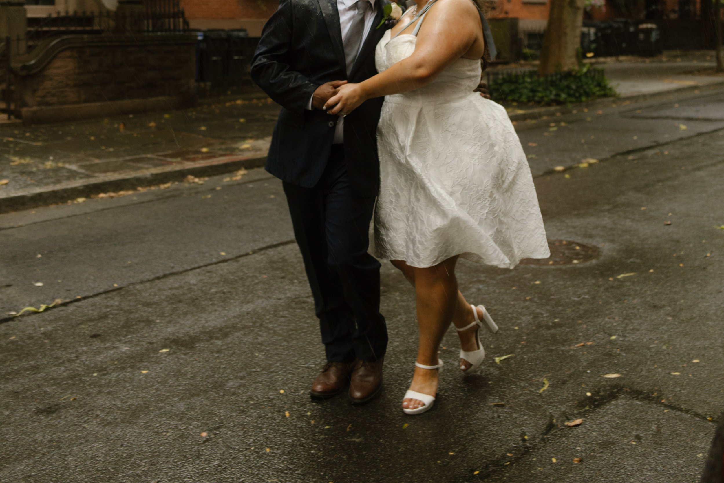 Newlyweds dance together in the rain on a quiet brownstone street after their intimate Wedding Locations in NYC celebration.