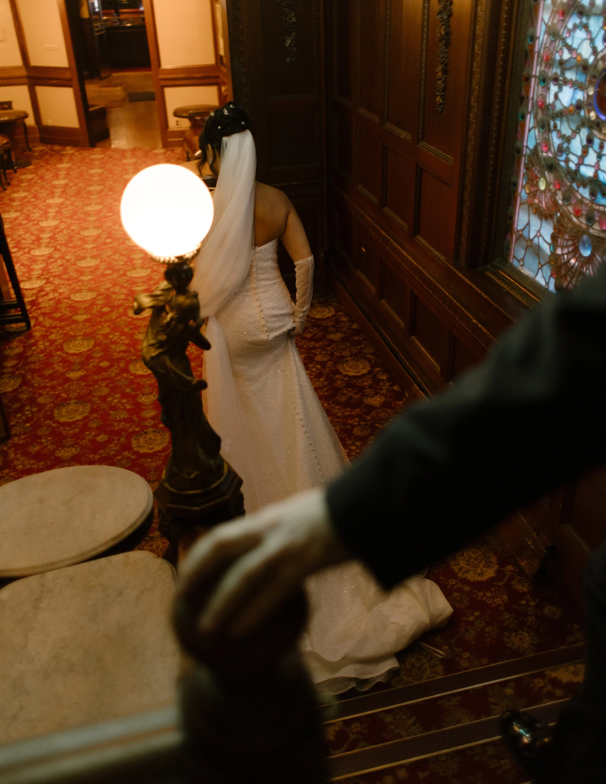 Bride walks through a historic hotel hallway with a flowing veil and elegant vintage architecture.