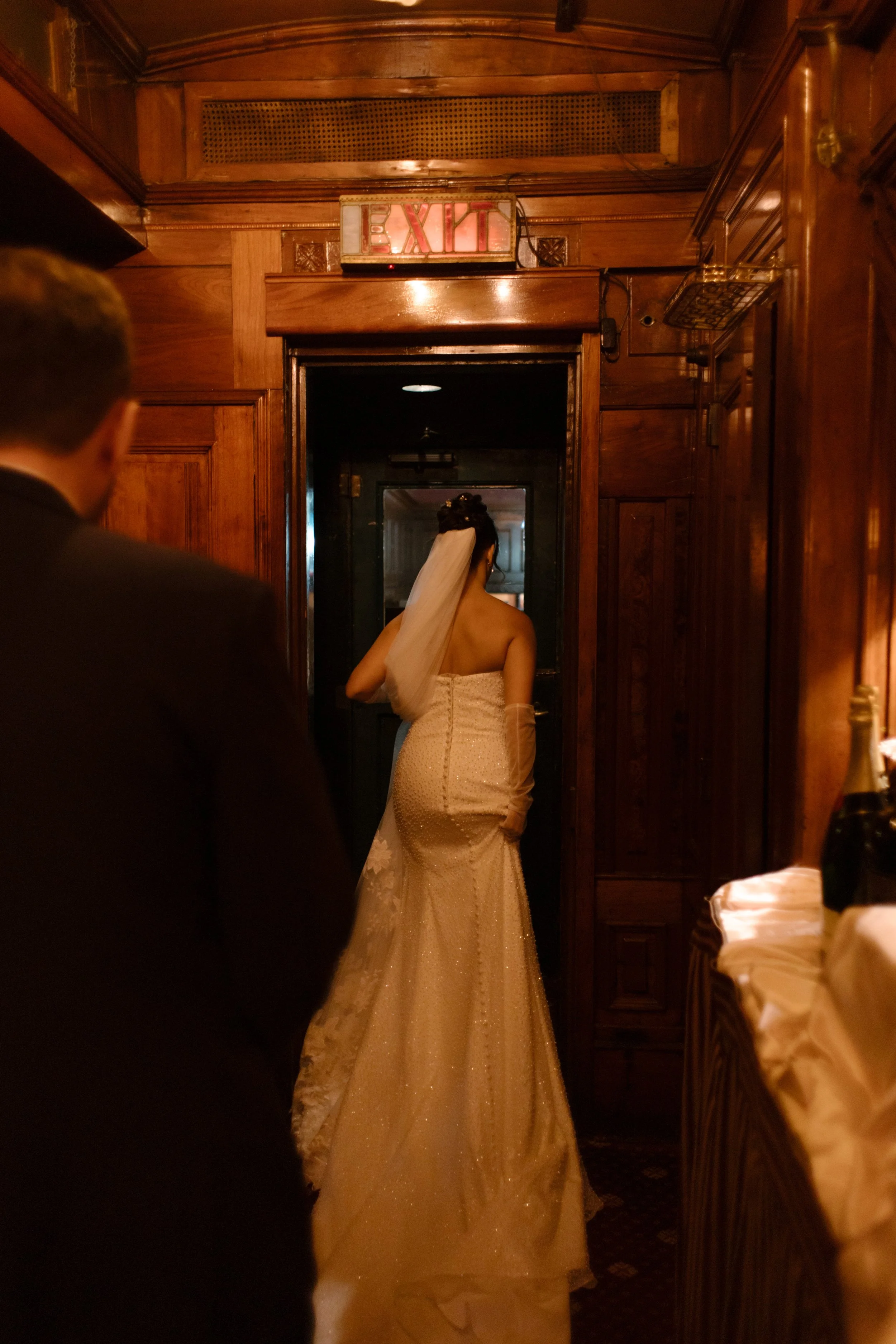 Bride walks toward the exit of a historic private dining railcar with her groom following close behind.