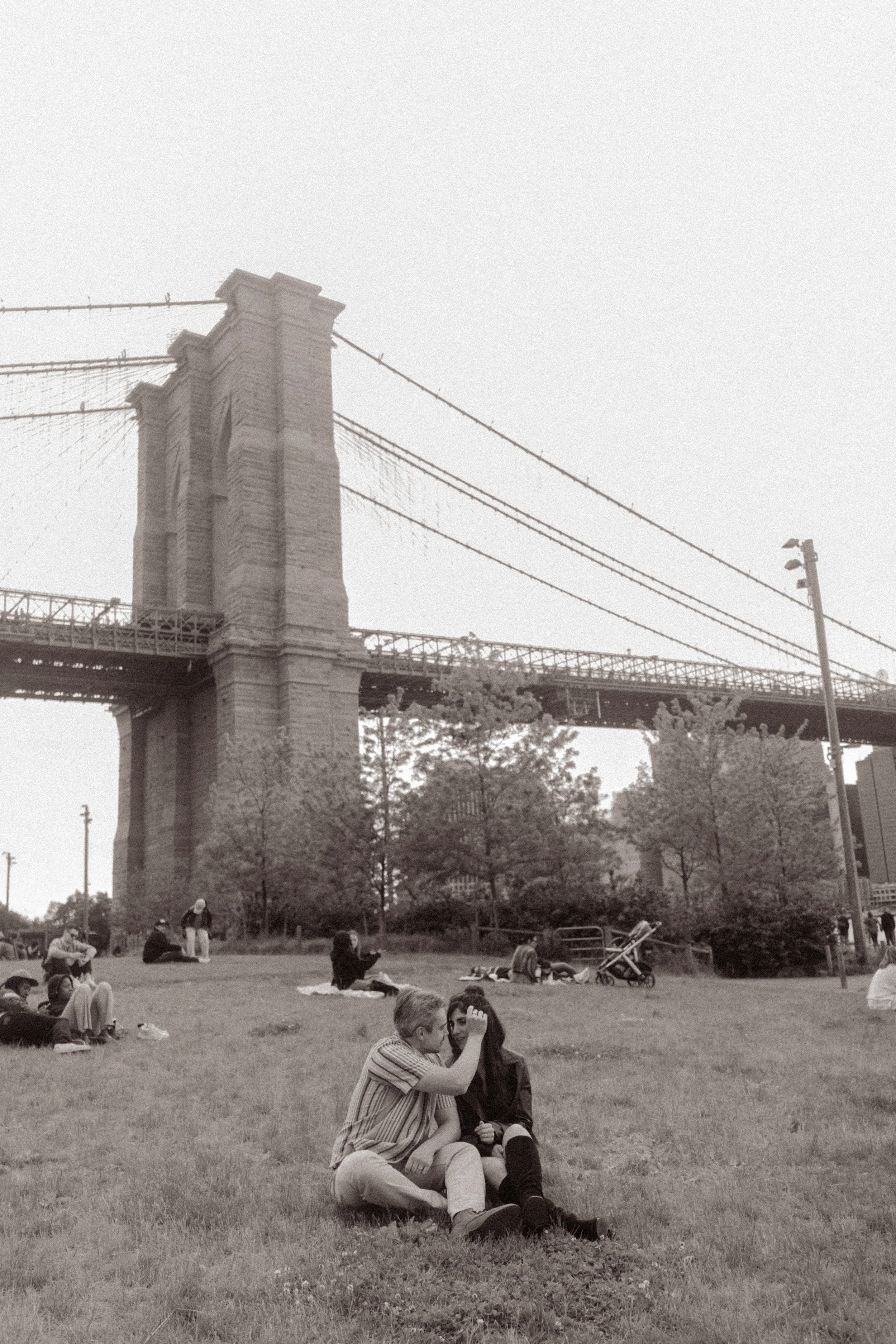 Couple sits together beneath the Brooklyn Bridge during a romantic engagement session at one of the most scenic Wedding Locations in NYC.