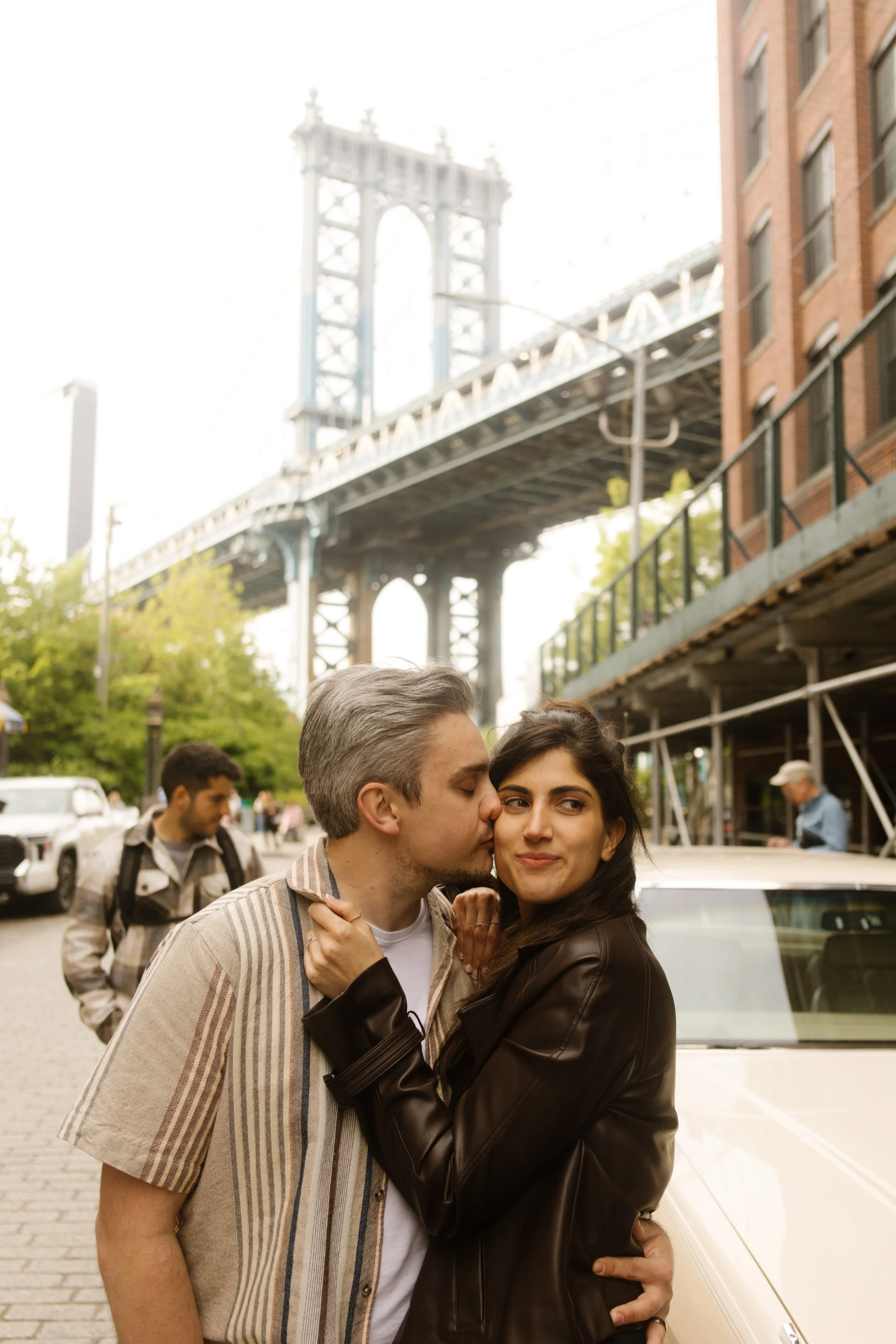 Couple shares a kiss beneath the Manhattan Bridge in DUMBO, one of the most iconic Wedding Locations in NYC for engagement photos.